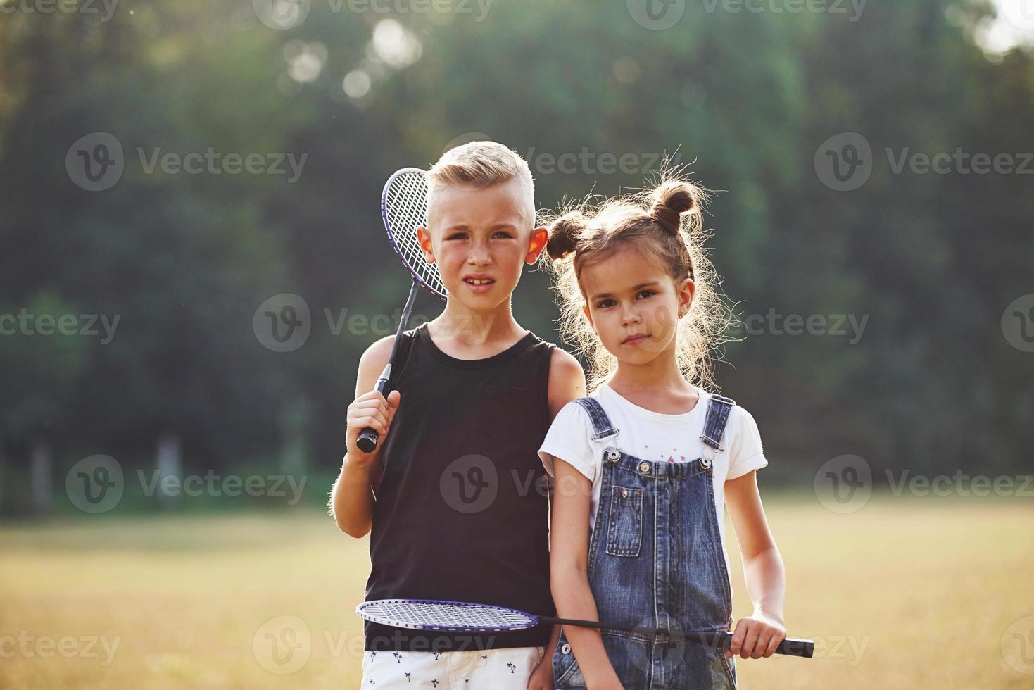 retrato de niño y niña que están parados en el campo en un día soleado con raquetas de tenis en las manos foto