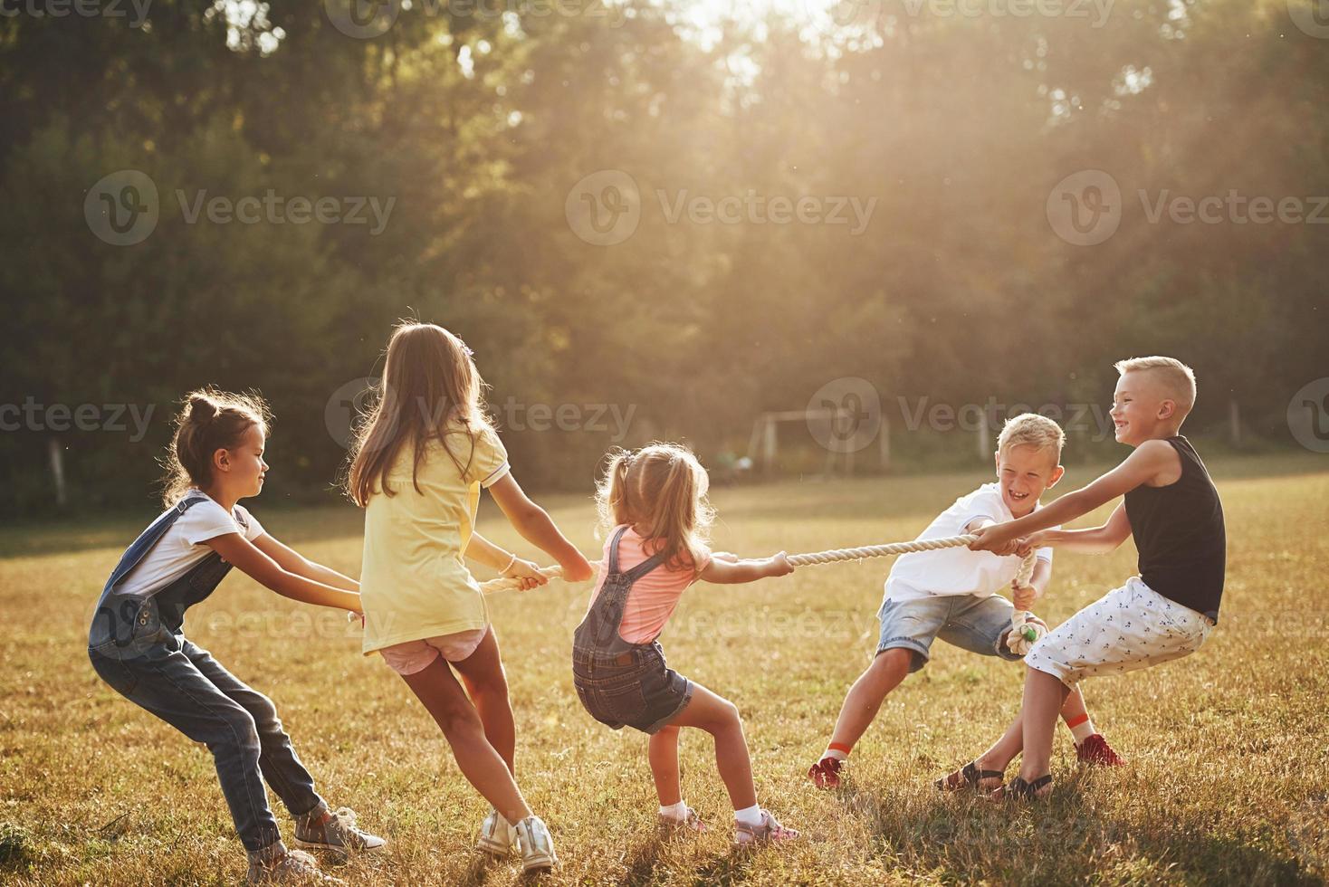 Kids playing tug of war game in the beautiful meadow at sunny day photo