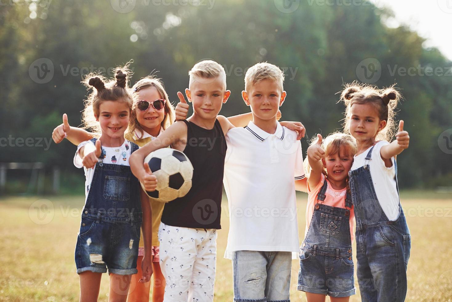 Young sportive kids with soccer ball stands together in the field at sunny day photo