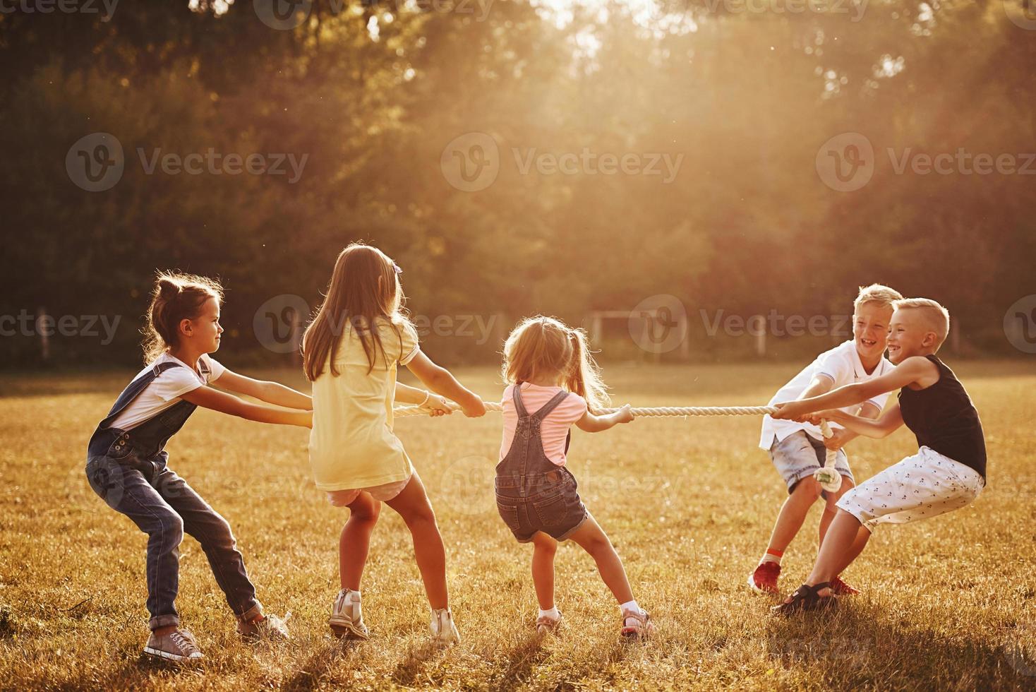 Kids playing tug of war game in the beautiful meadow at sunny day photo