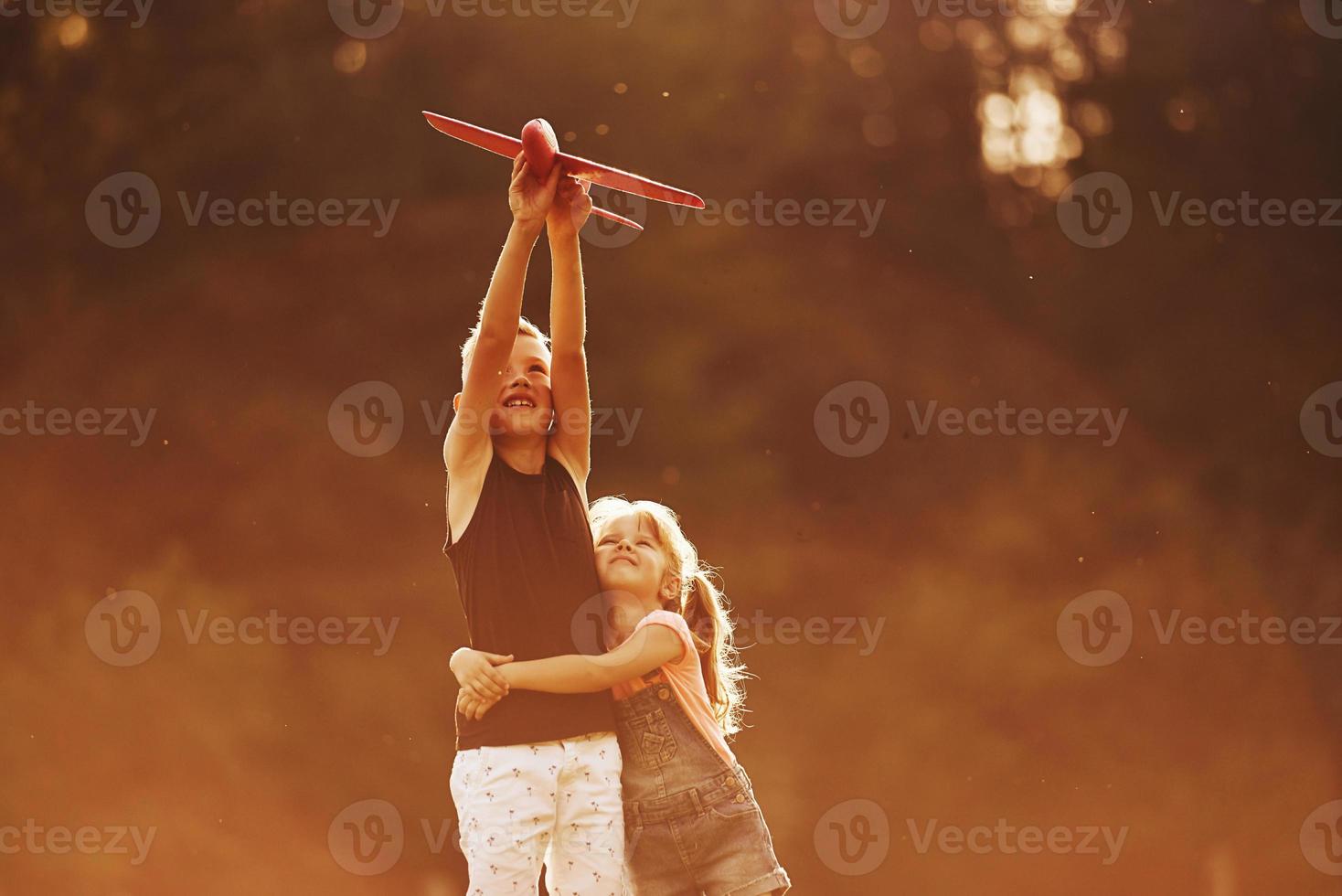 Girl and boy having fun outdoors with red toy airplane in hands photo