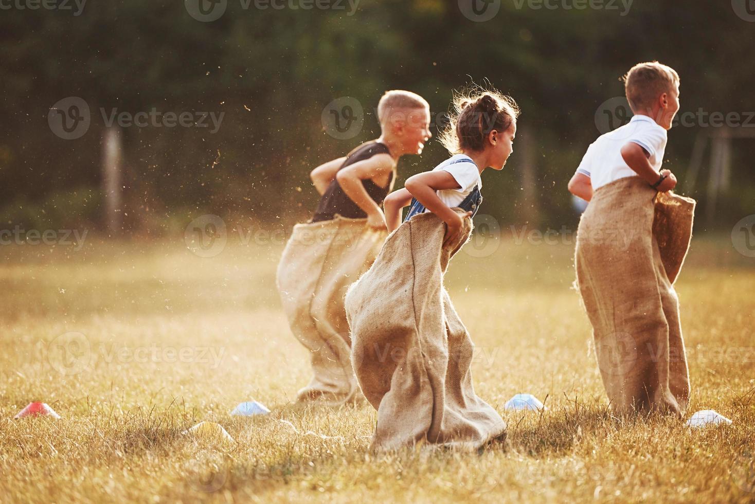 saltando carrera de sacos al aire libre en el campo. los niños se divierten durante el día soleado foto