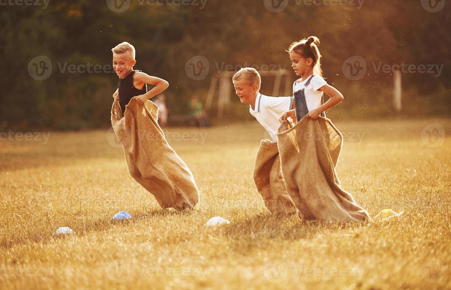 saltando carrera de sacos al aire libre en el campo. los niños se divierten durante el día soleado foto