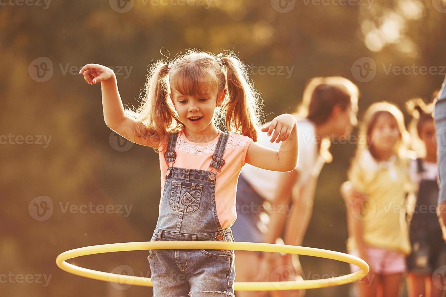 chica con herramienta de fitness circular. grupo de niños tiene un fin de semana activo en el campo. iluminado por la hermosa luz del sol foto