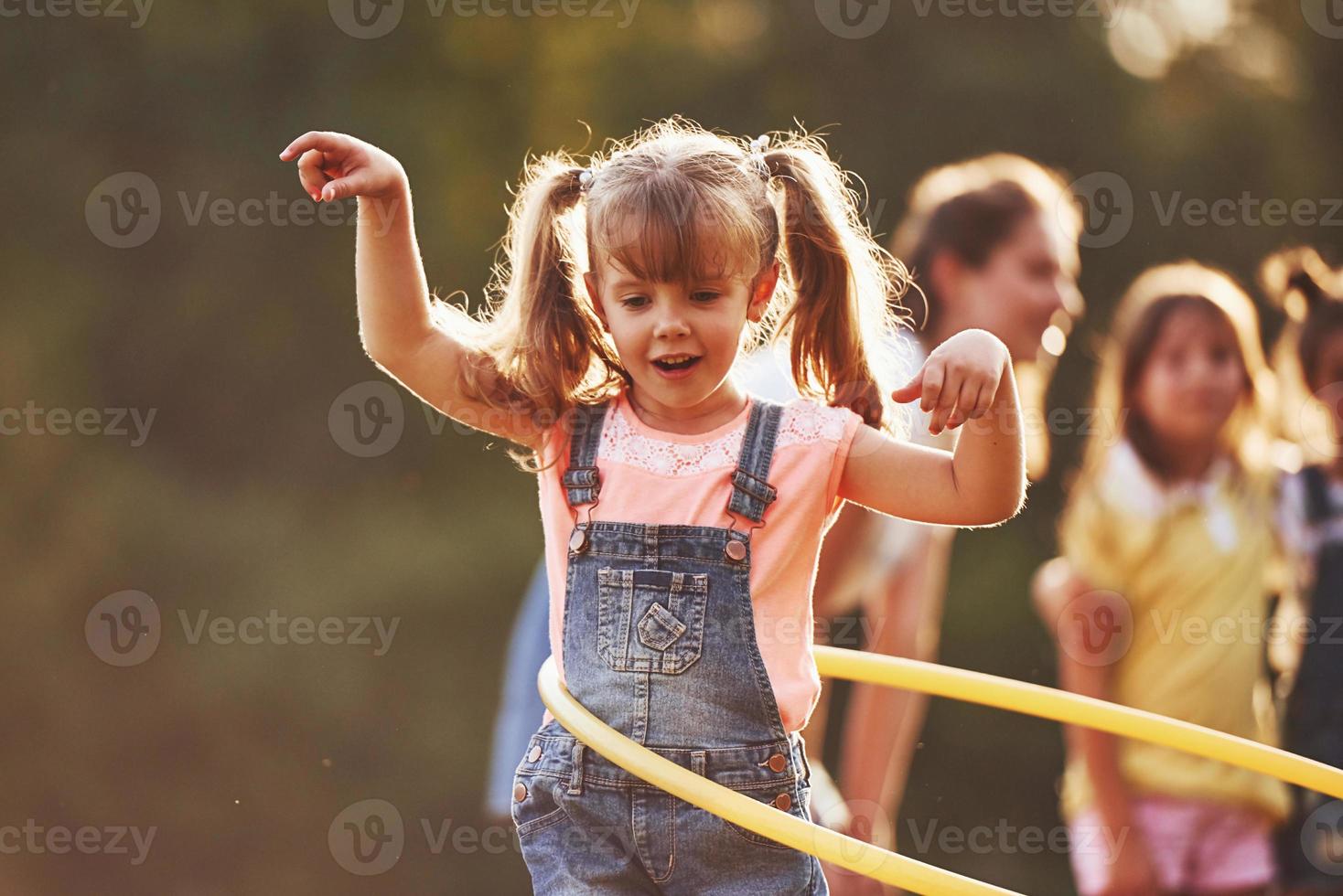 chica con herramienta de fitness circular. grupo de niños tiene un fin de semana activo en el campo. iluminado por la hermosa luz del sol foto