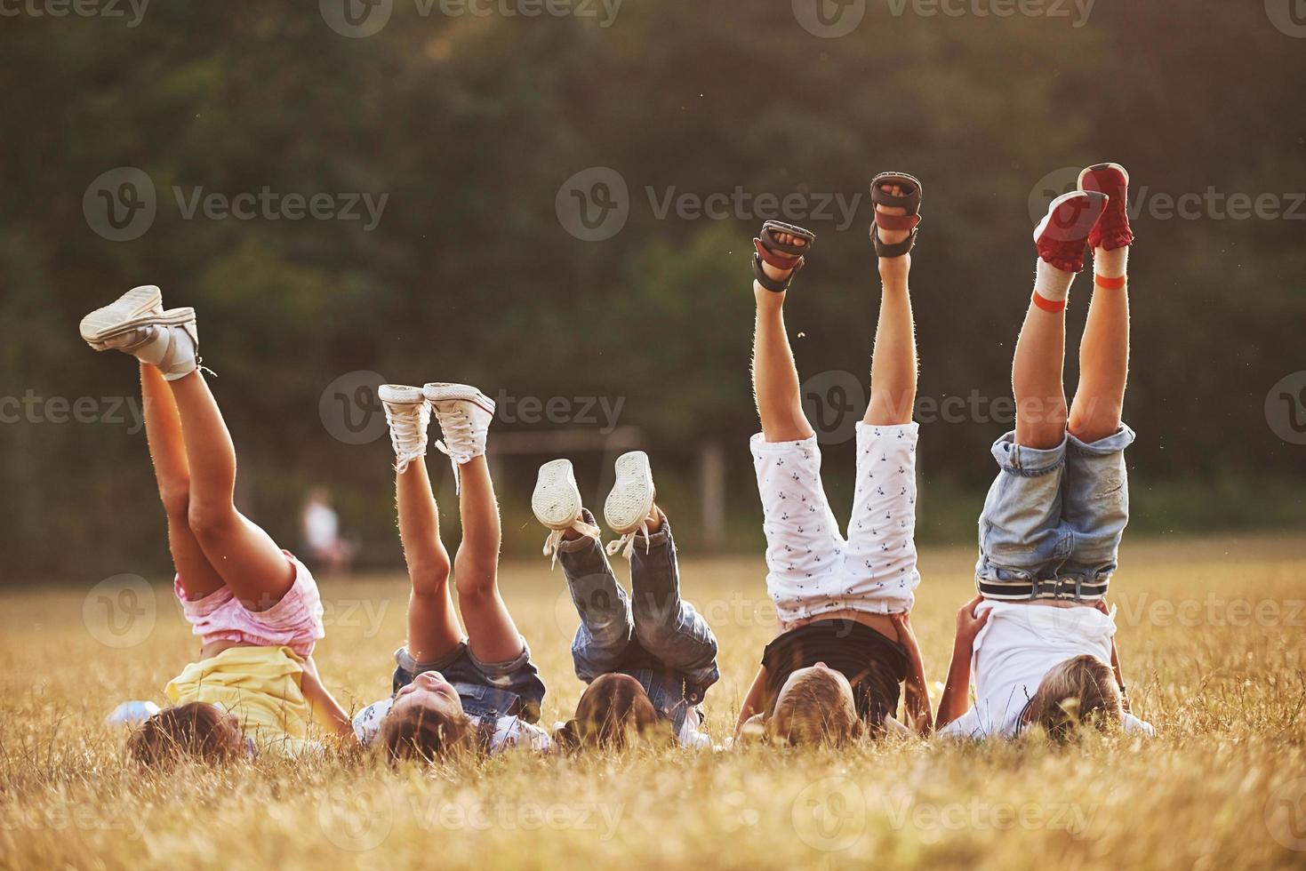 niños descansando juntos en el campo durante el día soleado. levantando las piernas foto