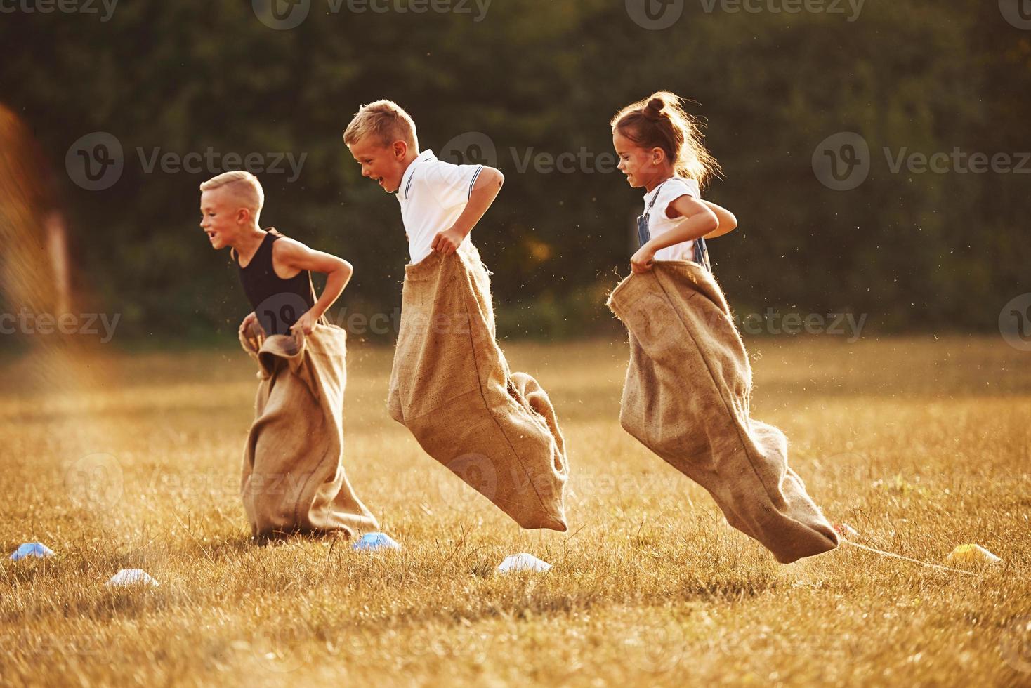 saltando carrera de sacos al aire libre en el campo. los niños se divierten durante el día soleado foto