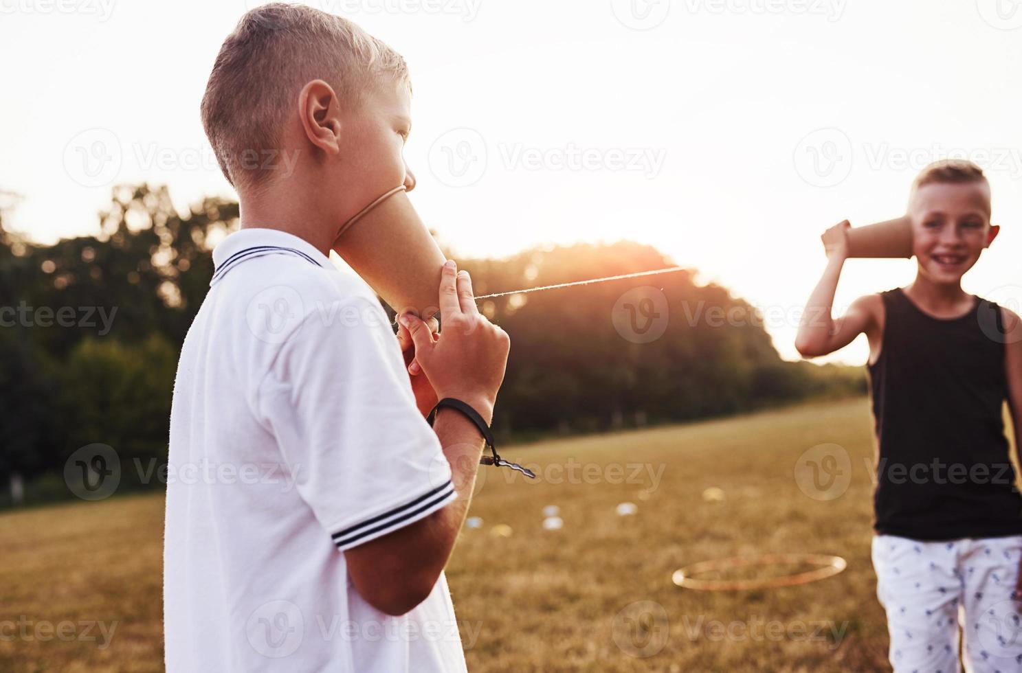 Two boys stands in the field and talking by using string can phone photo