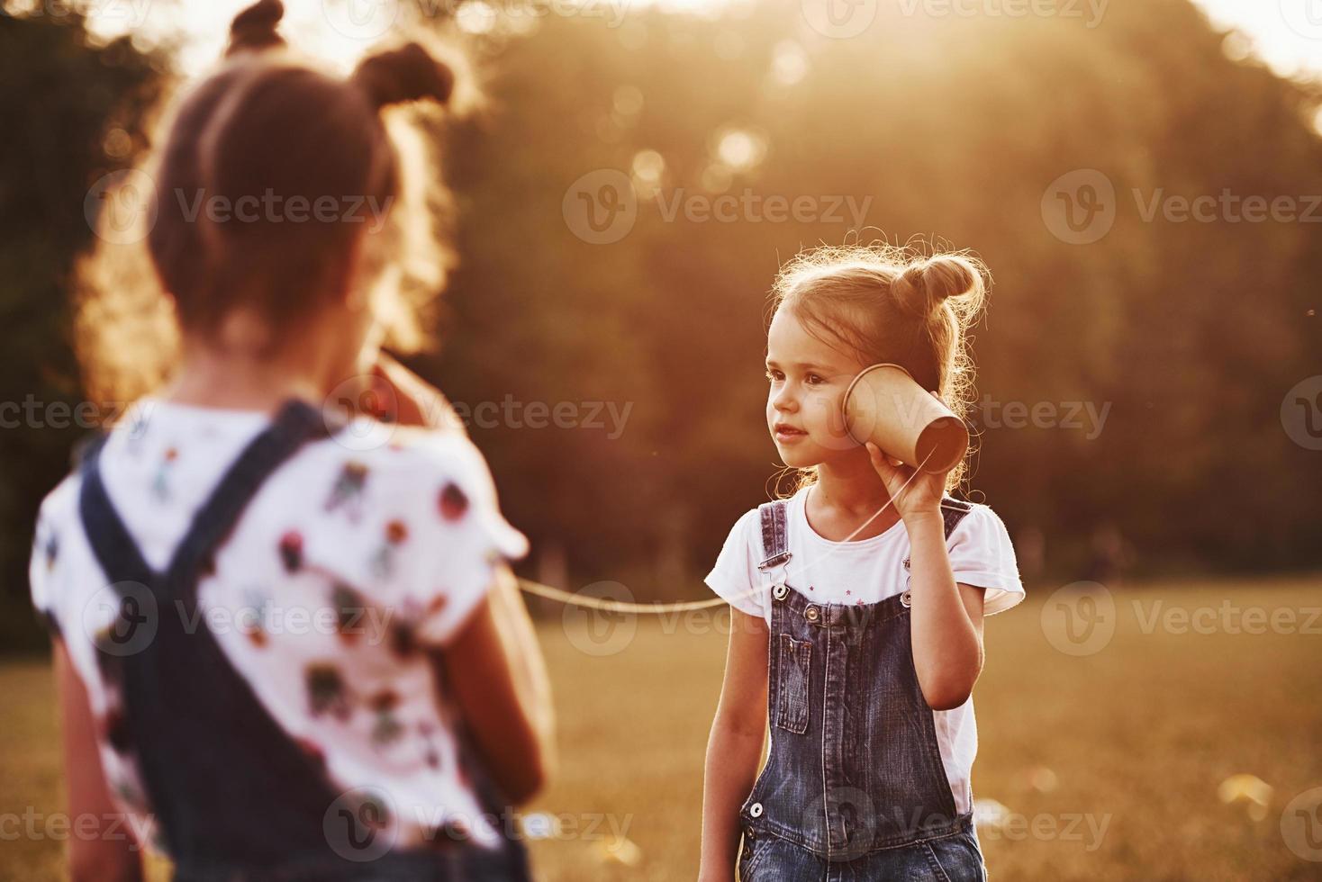 dos niñas se paran en el campo y hablan usando una cuerda por teléfono foto