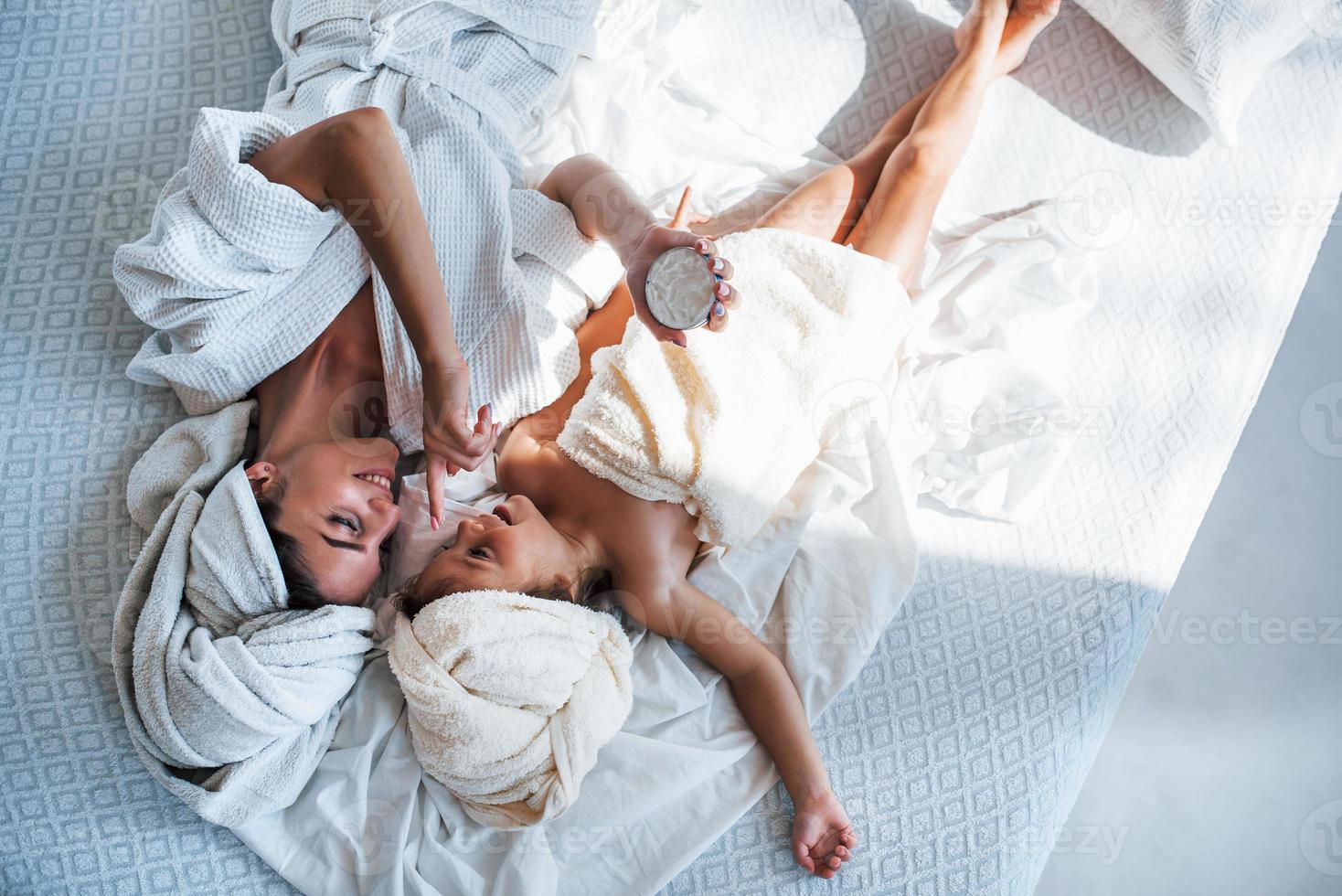 vista superior. usando crema. la joven madre con su hija tiene un día de belleza en el interior de la habitación blanca foto