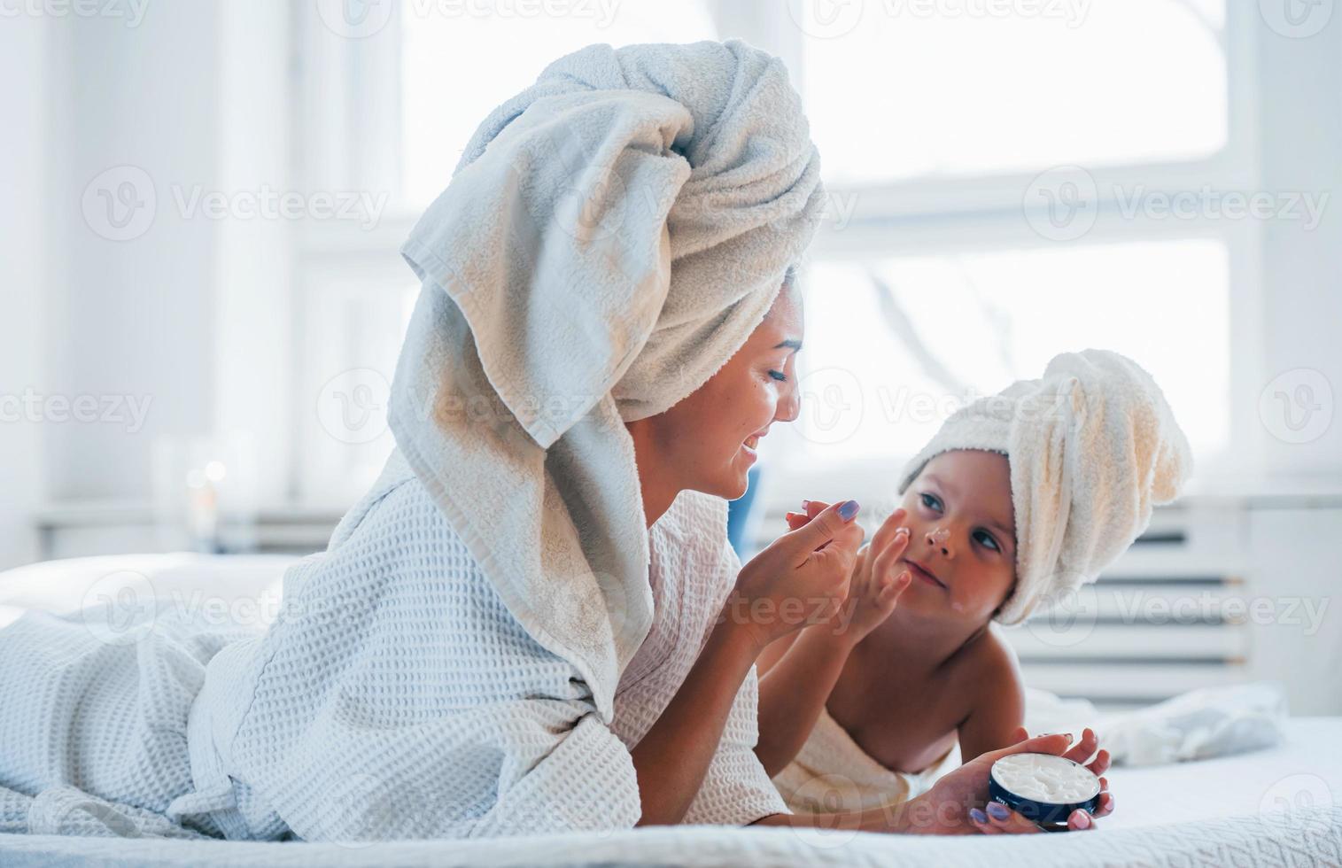 Using cream. Young mother with her daugher have beauty day indoors in white room photo