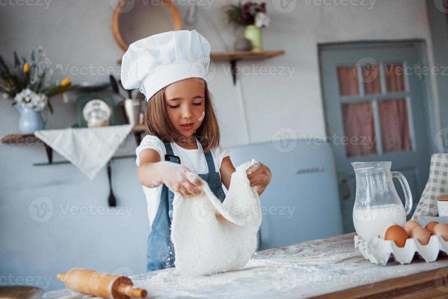 niño lindo con uniforme de chef blanco preparando comida en la cocina foto