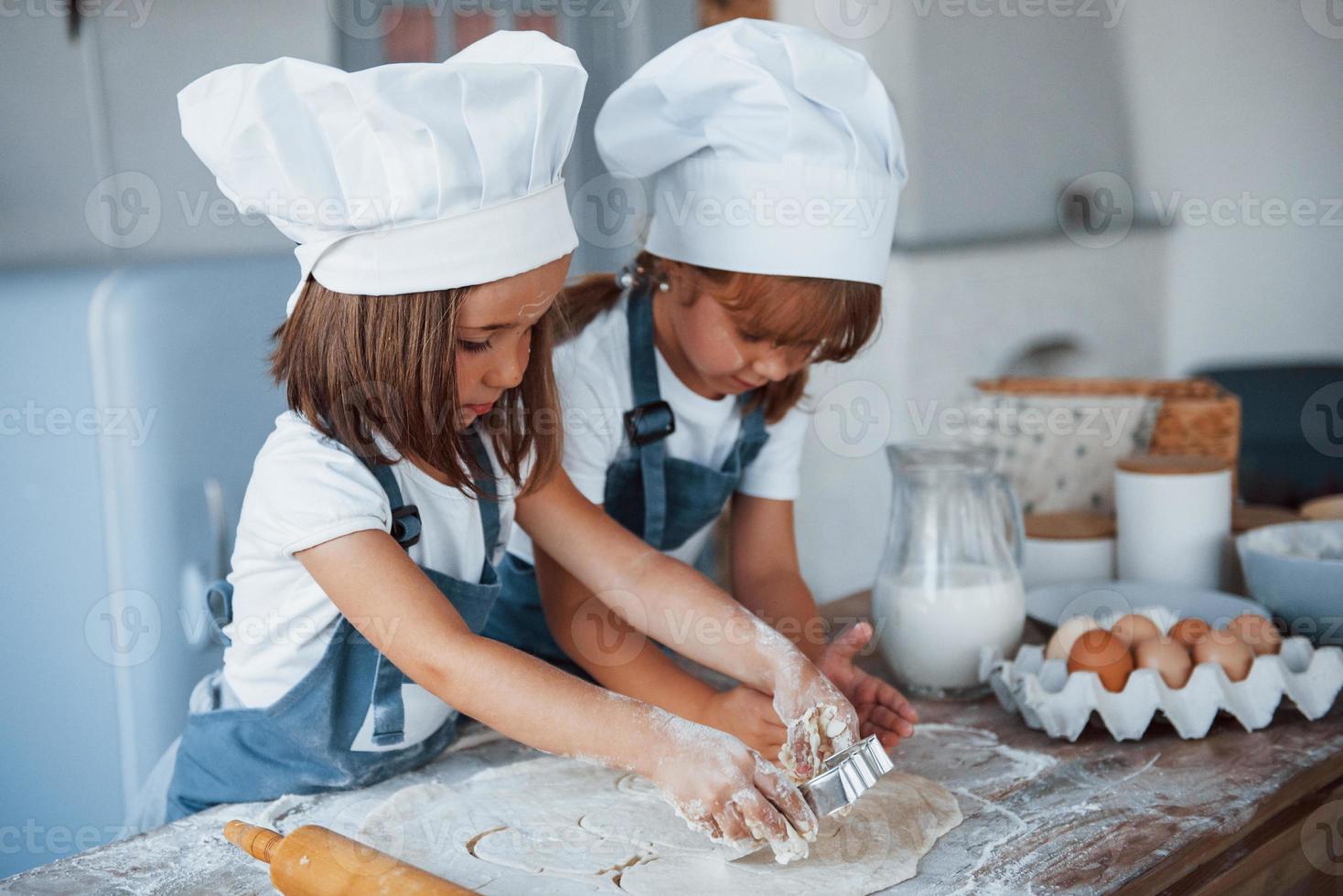 Concentrating at cooking. Family kids in white chef uniform preparing food on the kitchen photo