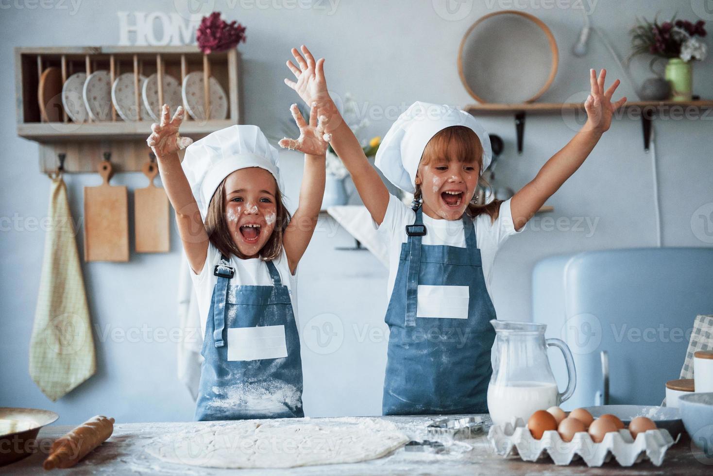 Having fun during the process. Family kids in white chef uniform preparing food on the kitchen photo