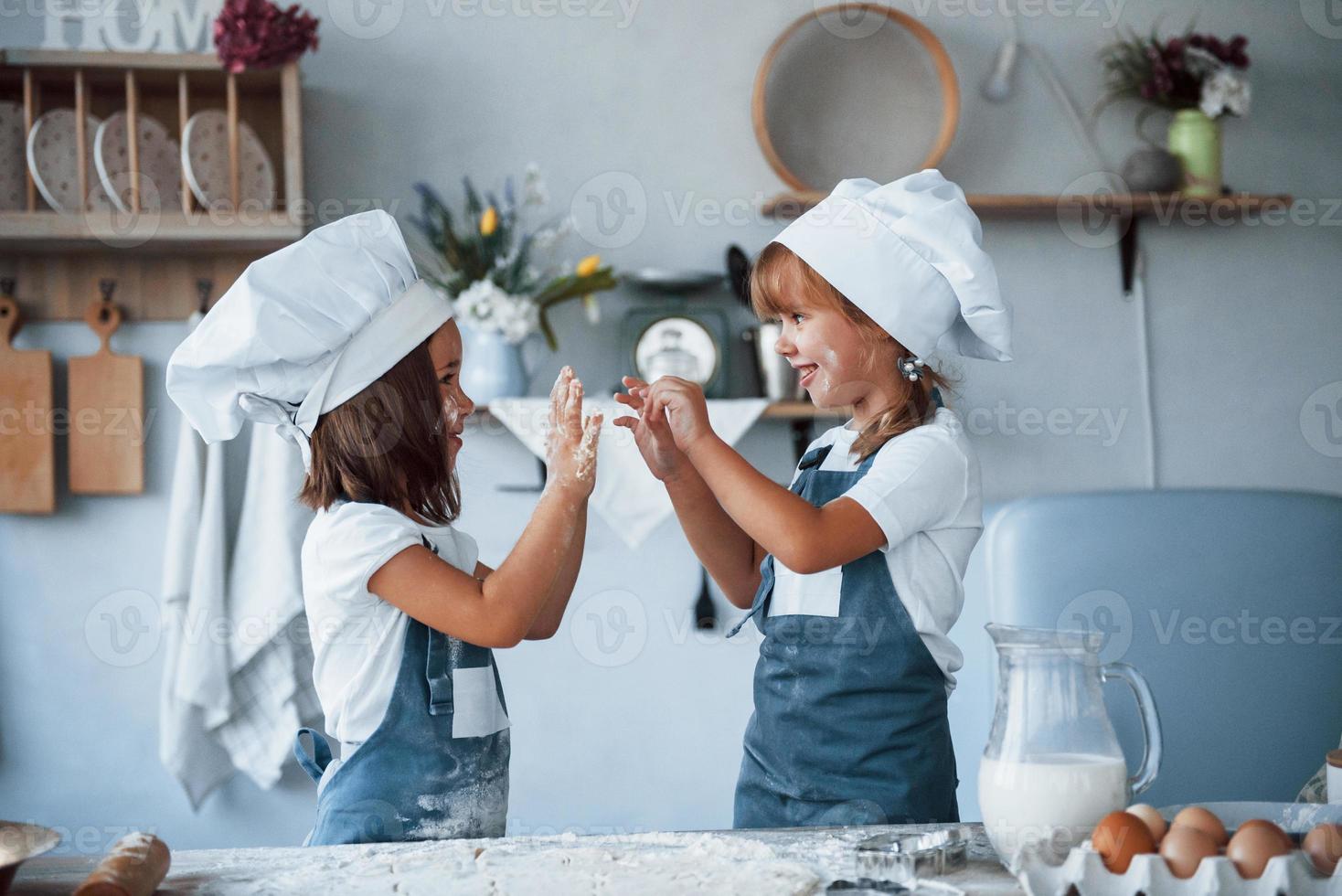 divertirse durante el proceso. niños de familia con uniforme de chef blanco preparando comida en la cocina foto