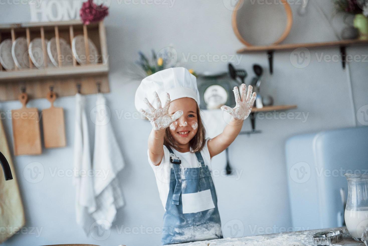 divirtiéndose. niño lindo con uniforme de chef blanco preparando comida en la cocina foto