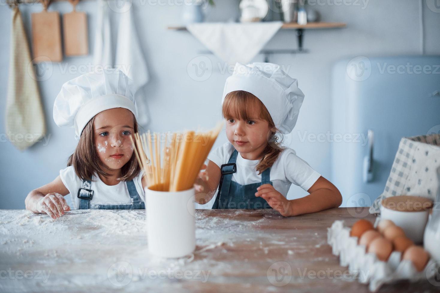 Having fun with spaghetti. Family kids in white chef uniform preparing food on the kitchen photo