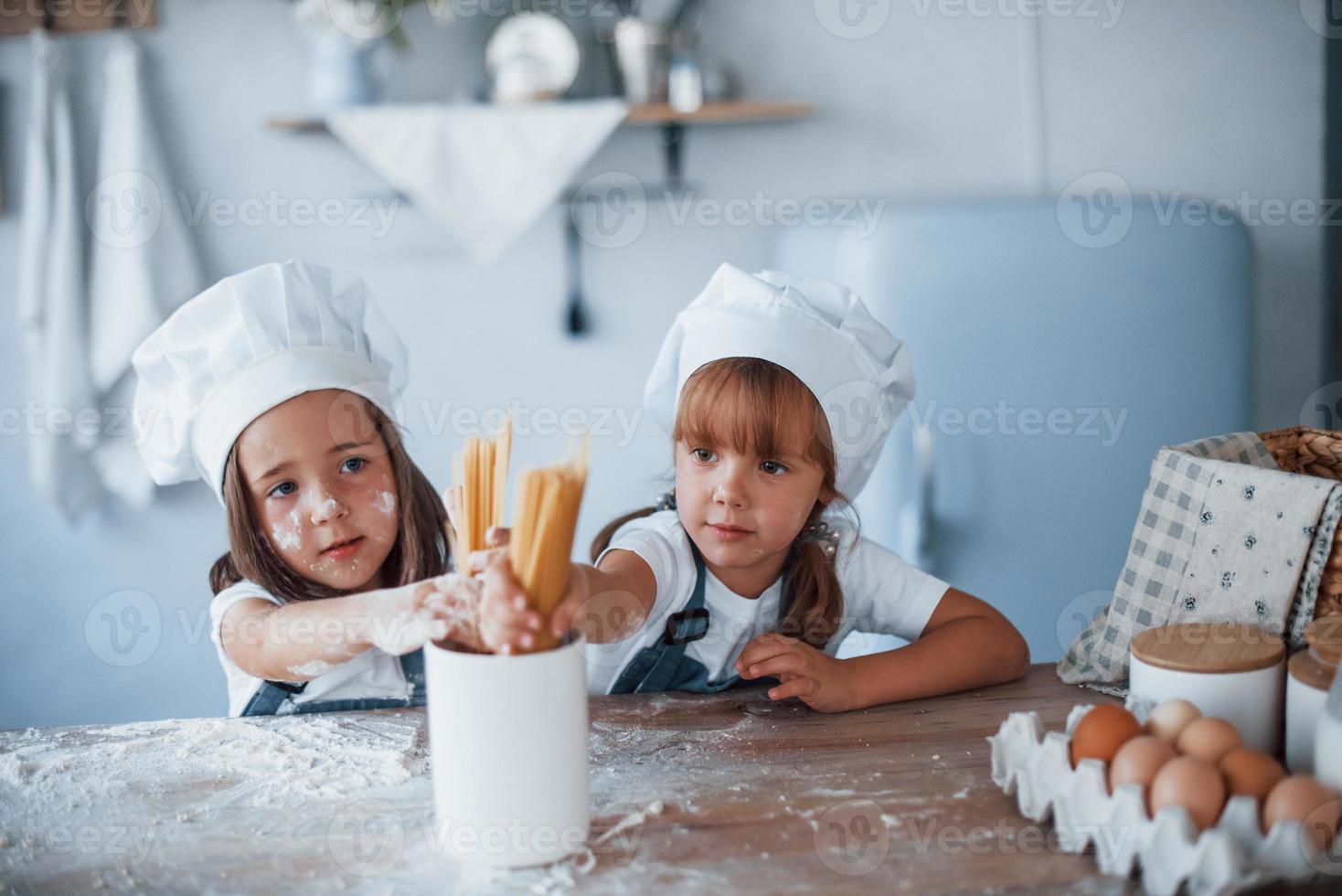 Having fun with spaghetti. Family kids in white chef uniform preparing food on the kitchen photo