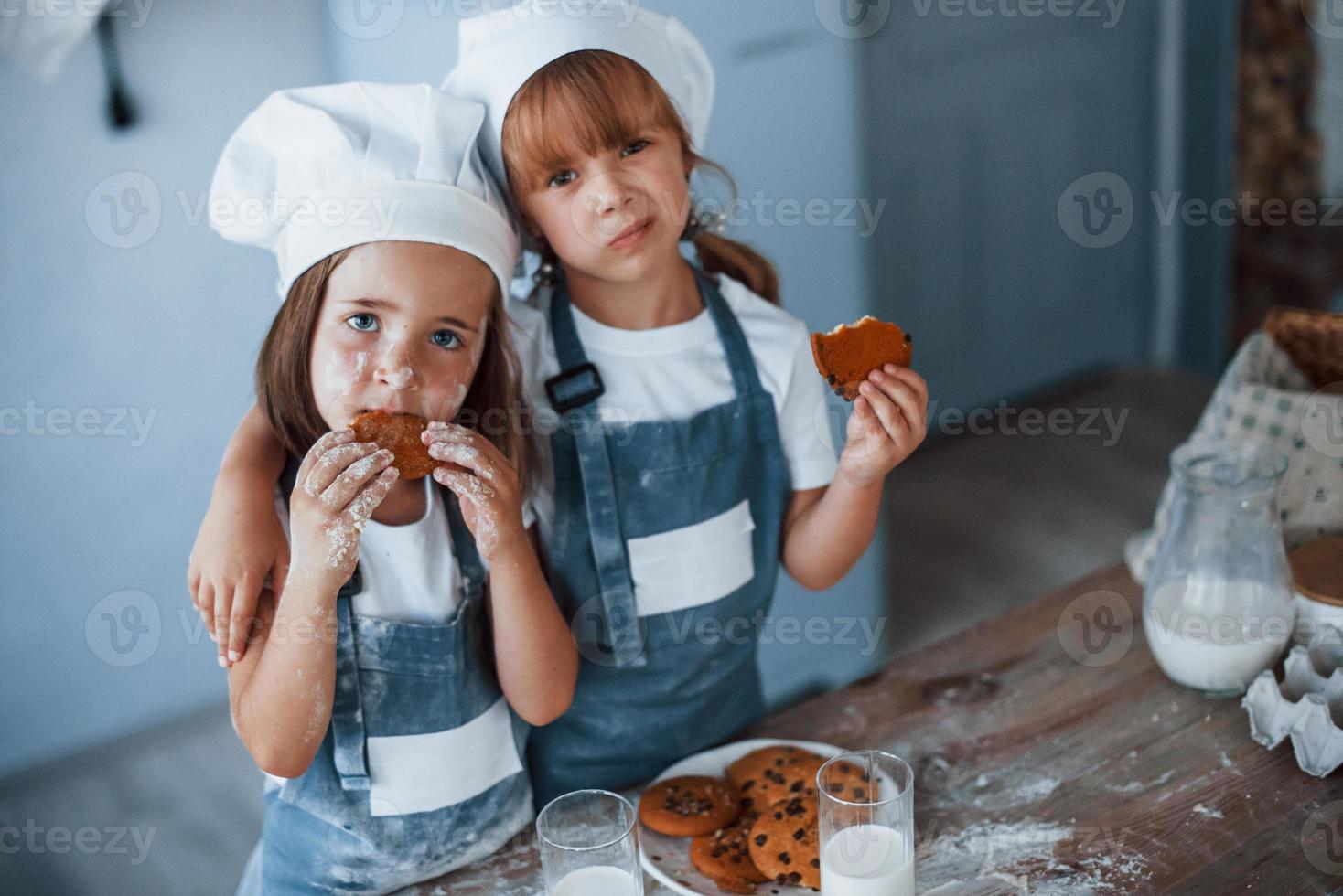 humor positivo. niños de familia con uniforme de chef blanco comiendo comida en la cocina foto