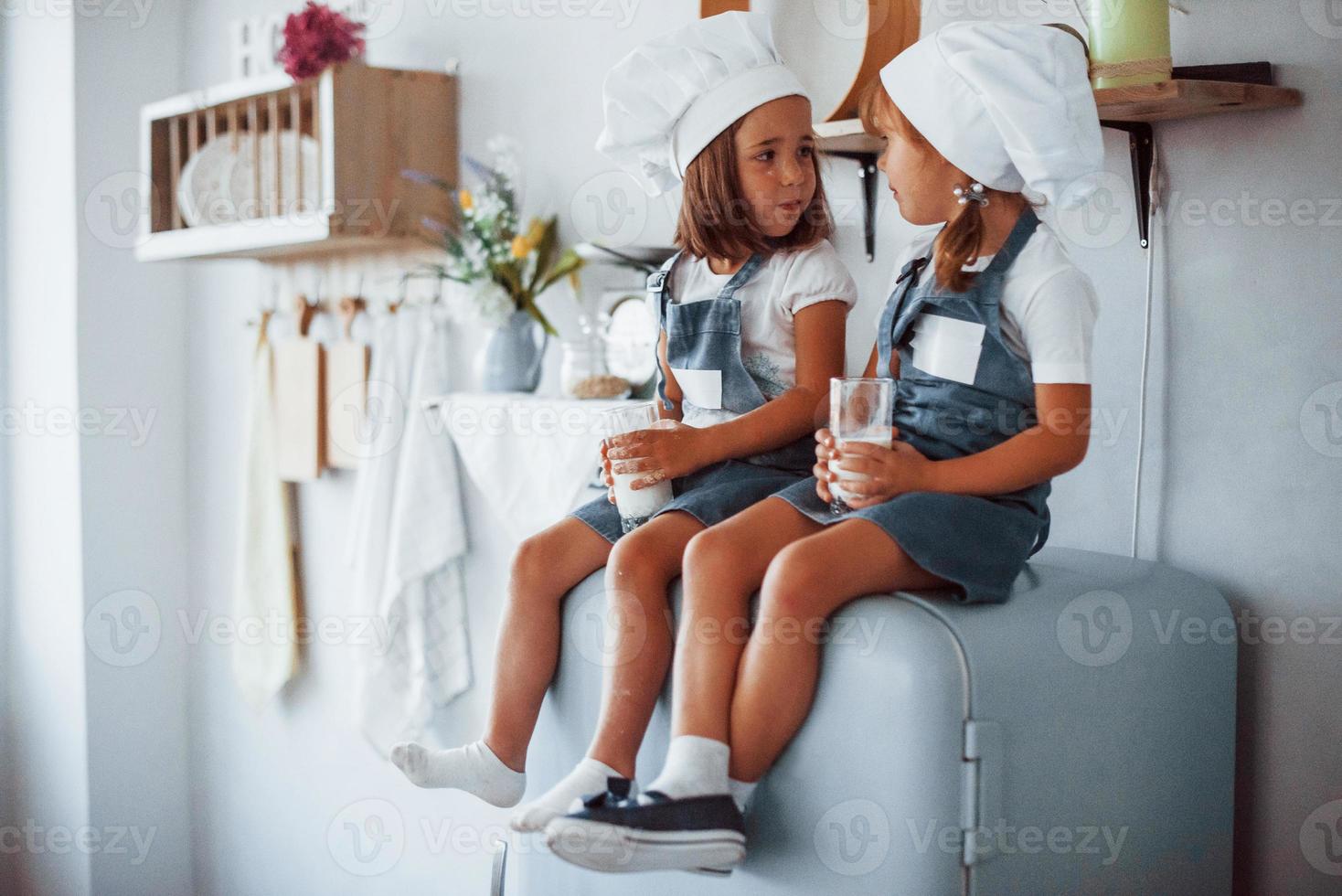 sentado en la nevera. los niños de la familia con uniforme de chef blanco comen comida en la cocina foto