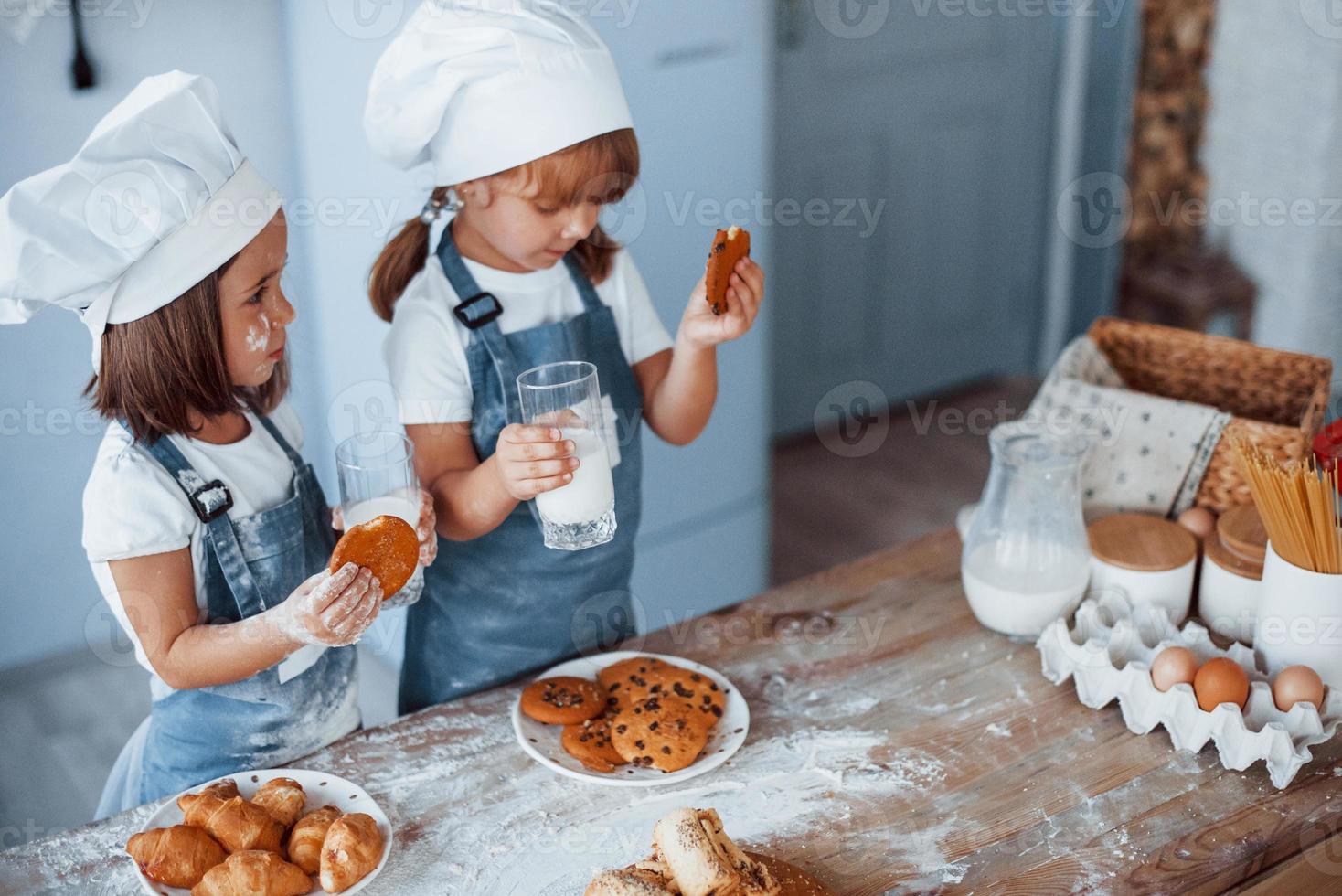 con vasos con leche. niños de familia con uniforme de chef blanco preparando comida en la cocina foto