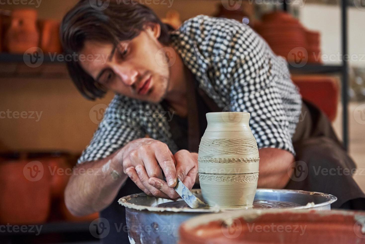 Makes lines with tool. Ceramist uses potter's wheel and creates a handmade clay product photo
