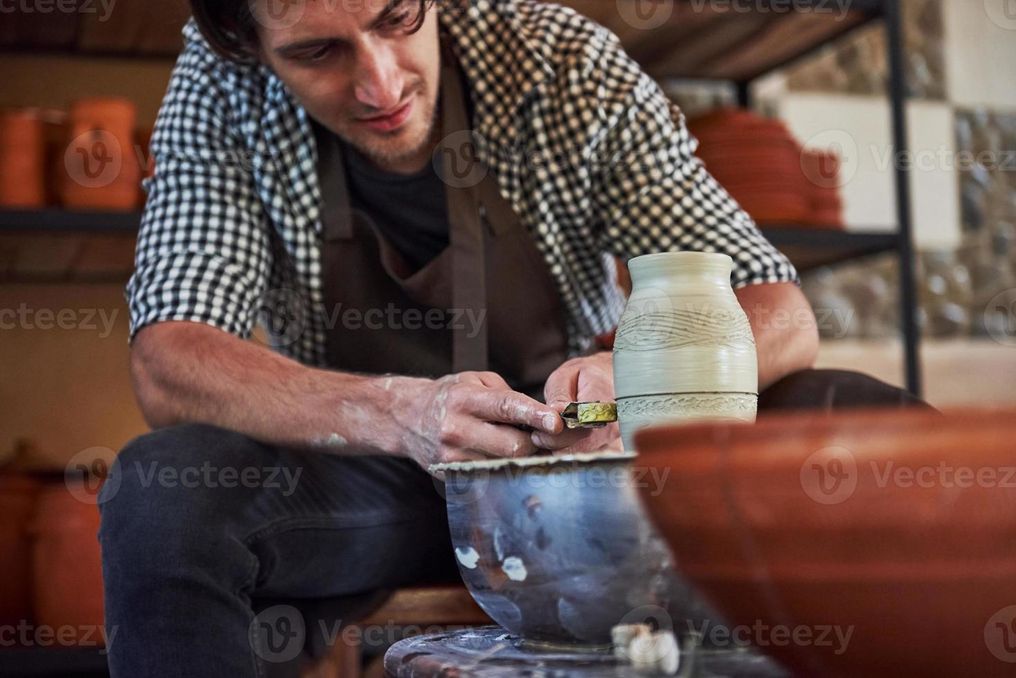 Makes lines with tool. Ceramist uses potter's wheel and creates a handmade clay product photo
