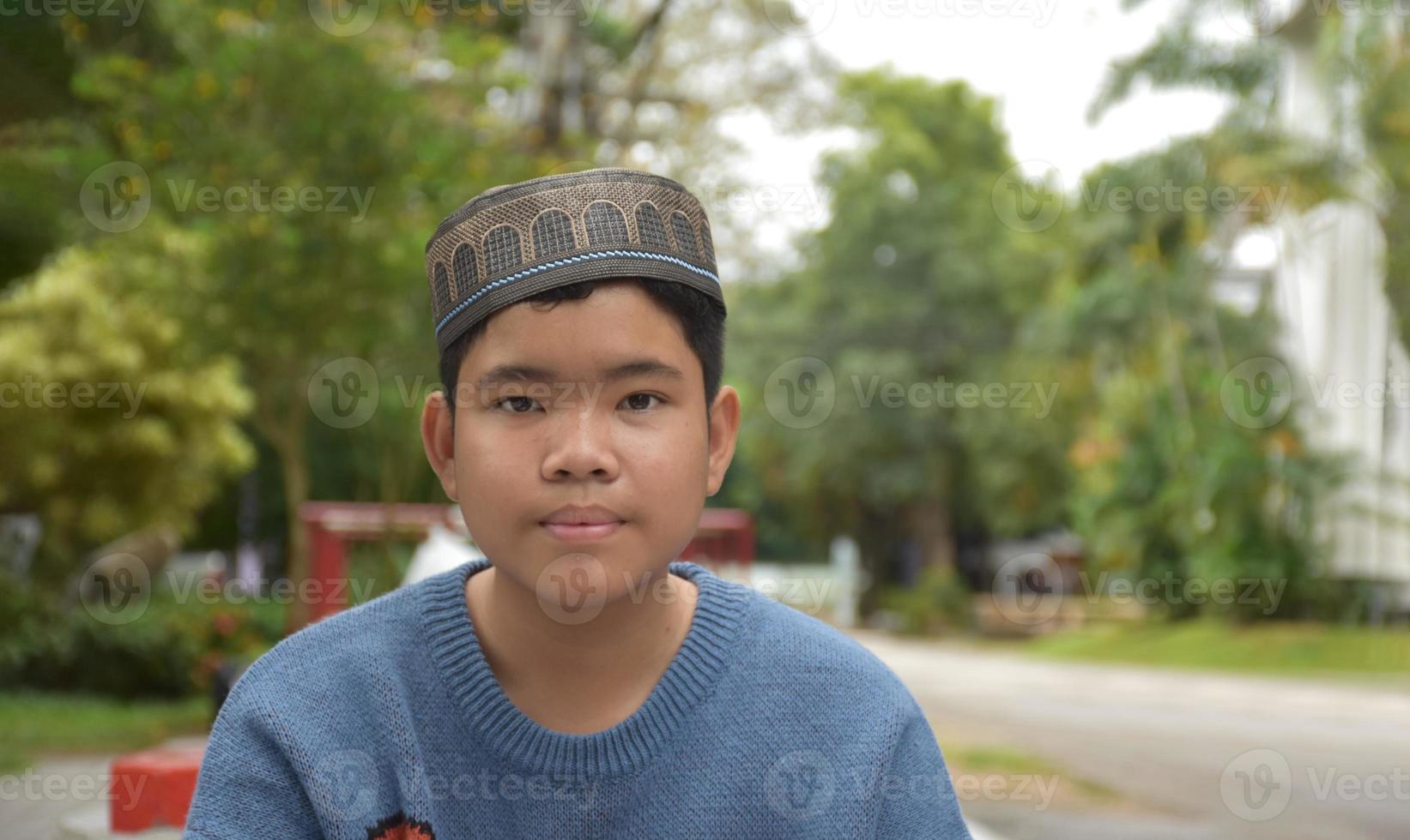 Portrait asian muslim or islamic boy sitting in the school park and smiling happily, soft and selective focus. photo