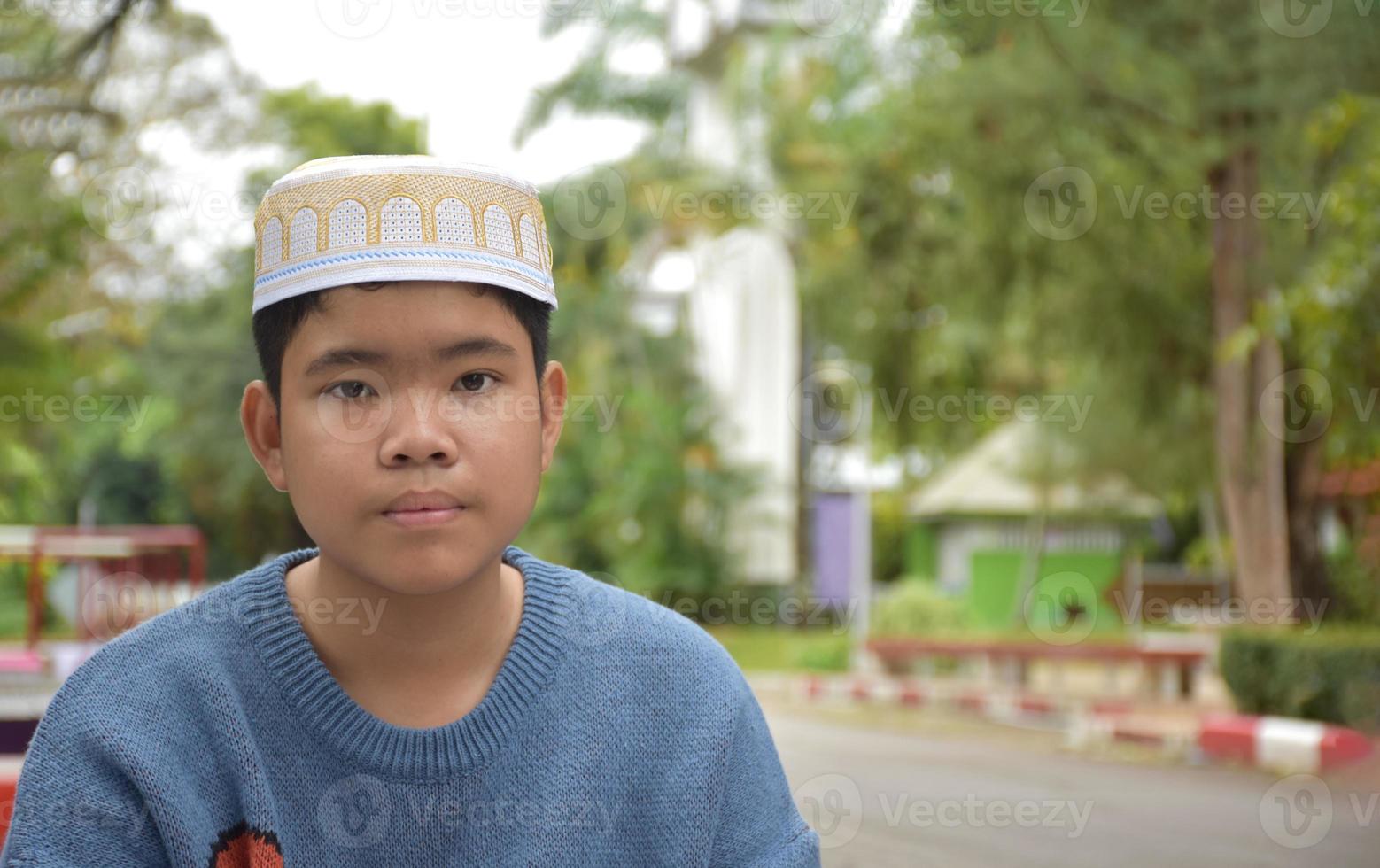 Portrait asian muslim or islamic boy sitting in the school park and smiling happily, soft and selective focus. photo