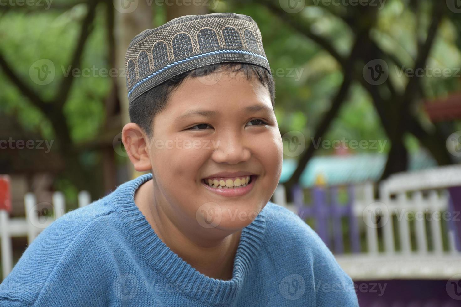 Portrait asian muslim or islamic boy sitting in the school park and smiling happily, soft and selective focus. photo