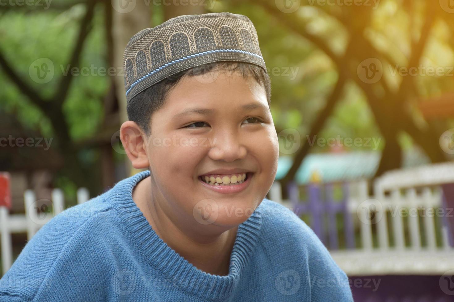 Portrait asian muslim or islamic boy sitting in the school park and smiling happily, soft and selective focus. photo