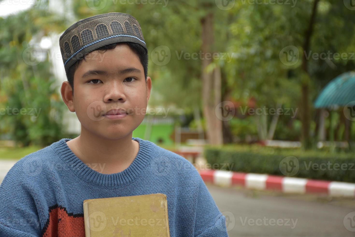 Portrait asian muslim or islamic boy sitting in the school park and smiling happily, soft and selective focus. photo