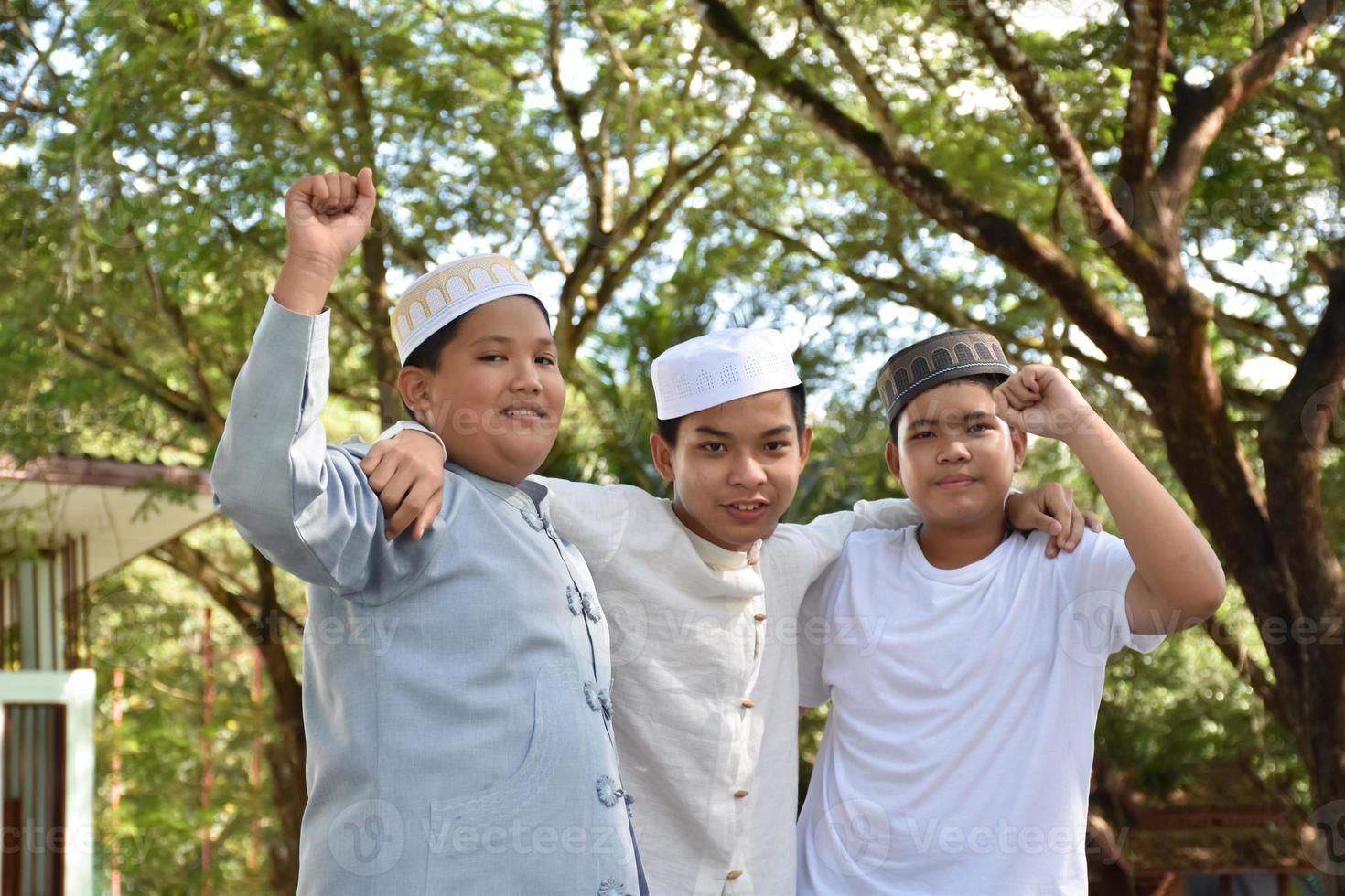 Young asian muslim boys raised hands, smilling and hugging each other to present happiness under the trees in the park, soft and selective focus. photo