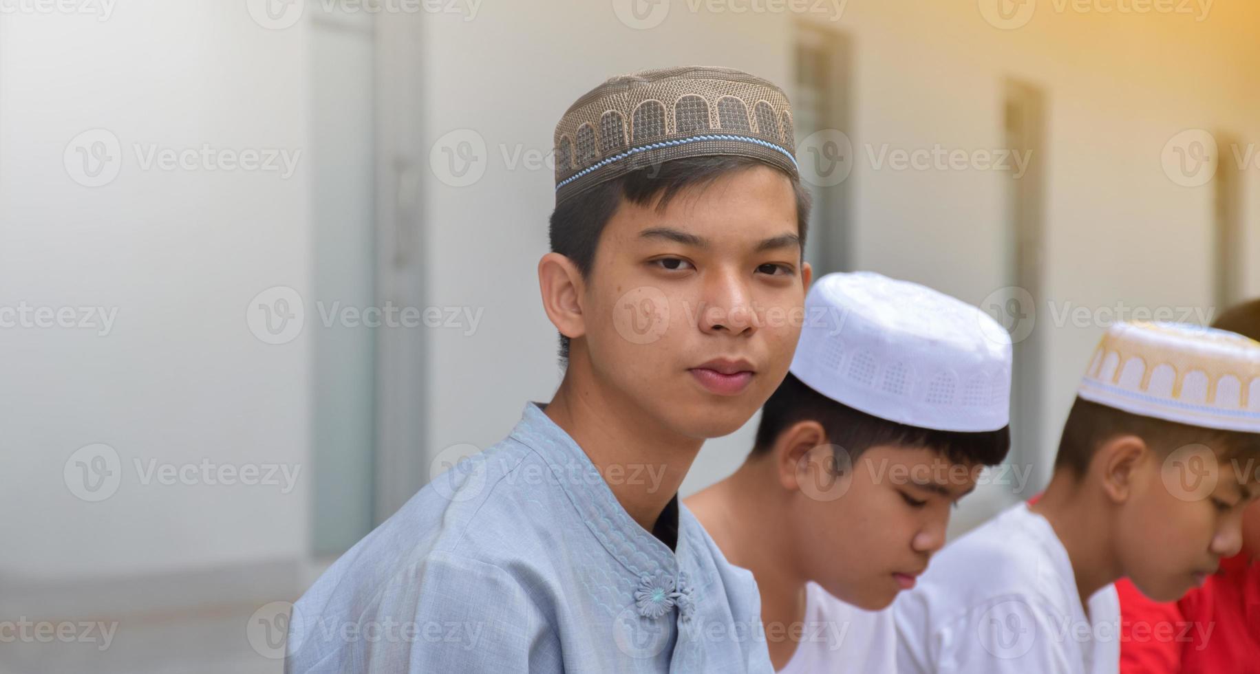 Portrait asian muslim or islamic boys sitting with muslim boys in a row to pray or to do the religious activity, soft and selective focus. photo