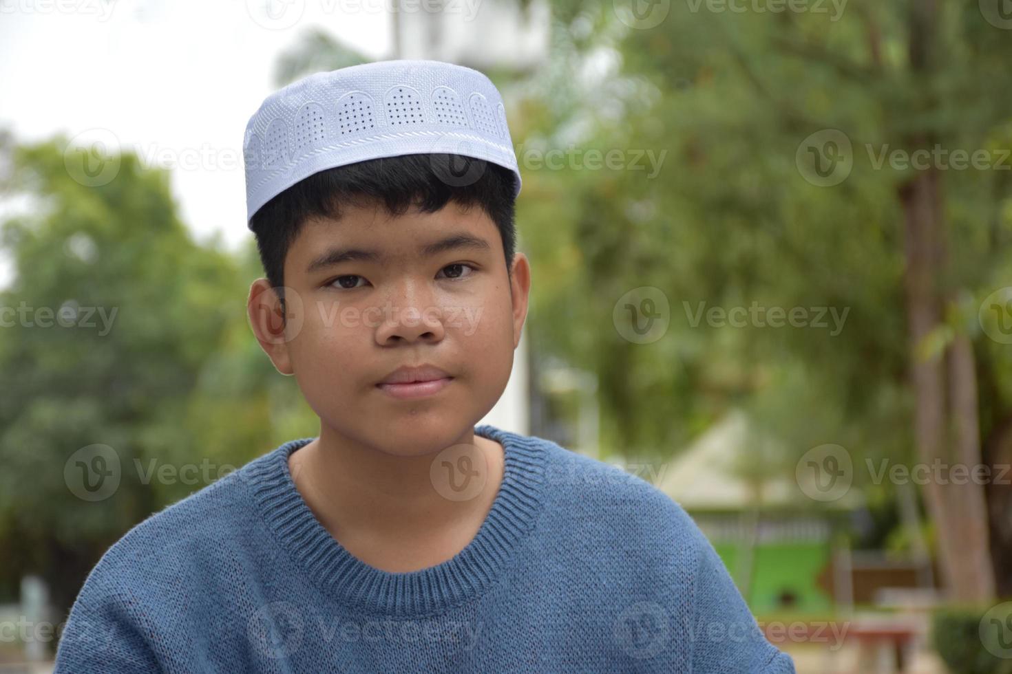 retrata a un niño musulmán o islámico asiático sentado en el parque escolar y sonriendo alegremente, con un enfoque suave y selectivo. foto