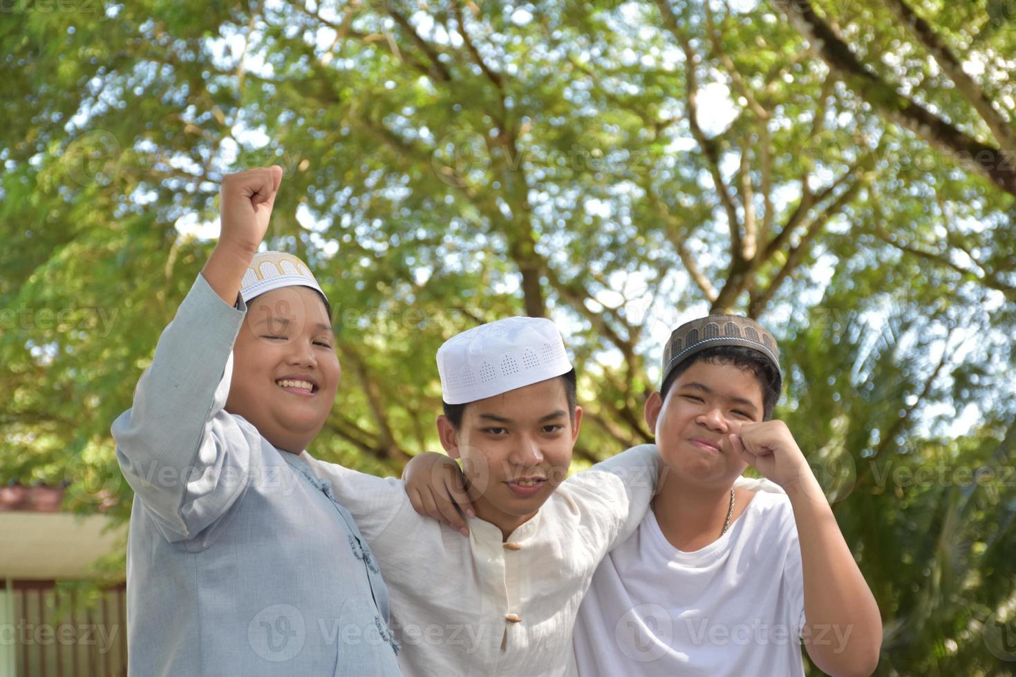 Young asian muslim boys raised hands, smilling and hugging each other to present happiness under the trees in the park, soft and selective focus. photo