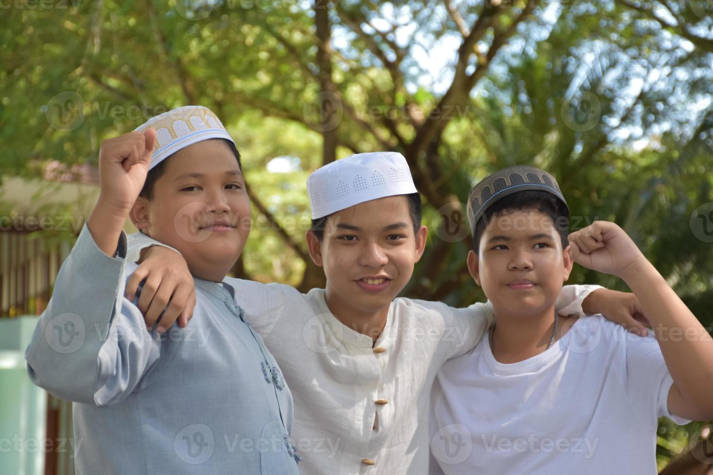 Young asian muslim boys raised hands, smilling and hugging each other to present happiness under the trees in the park, soft and selective focus. photo