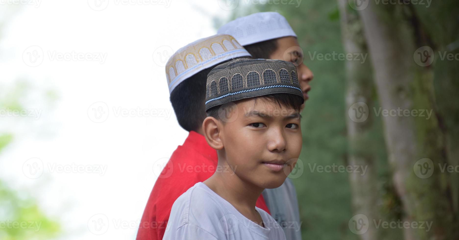 Portrait asian muslim or islamic boys standing together in front of tree and waiting to do the religious activity at school, soft and selective focus. photo