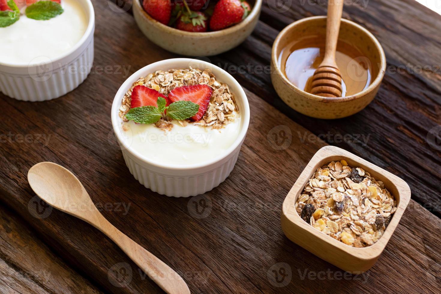 Strawberry yogurt in a wooden bowl with granola, honey, mint and fresh strawberry on wooden background. Health food concept. photo