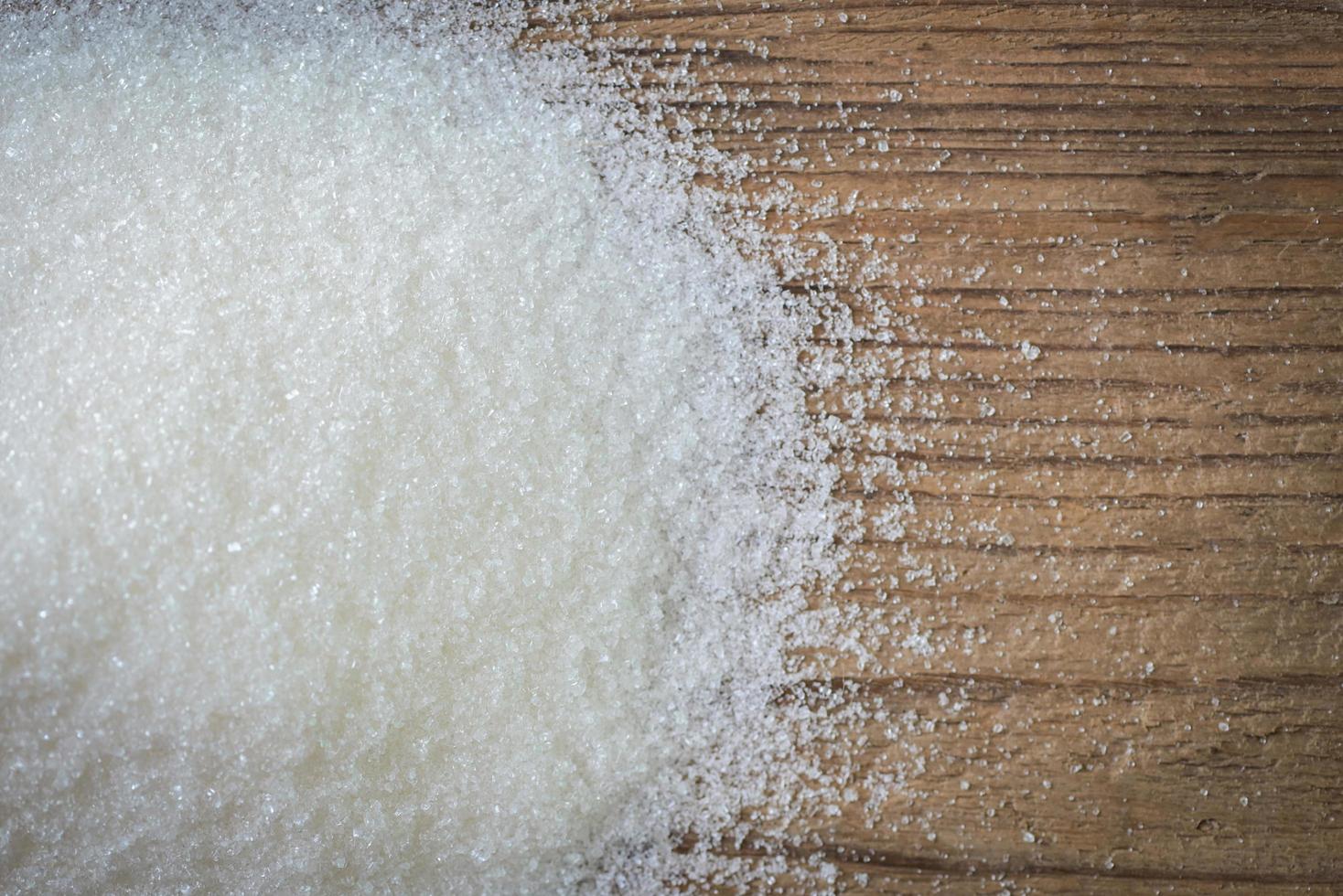 azúcar sobre fondo de madera, azúcar blanco para alimentos y dulces postres dulces montón de azúcar dulce granulado cristalino foto