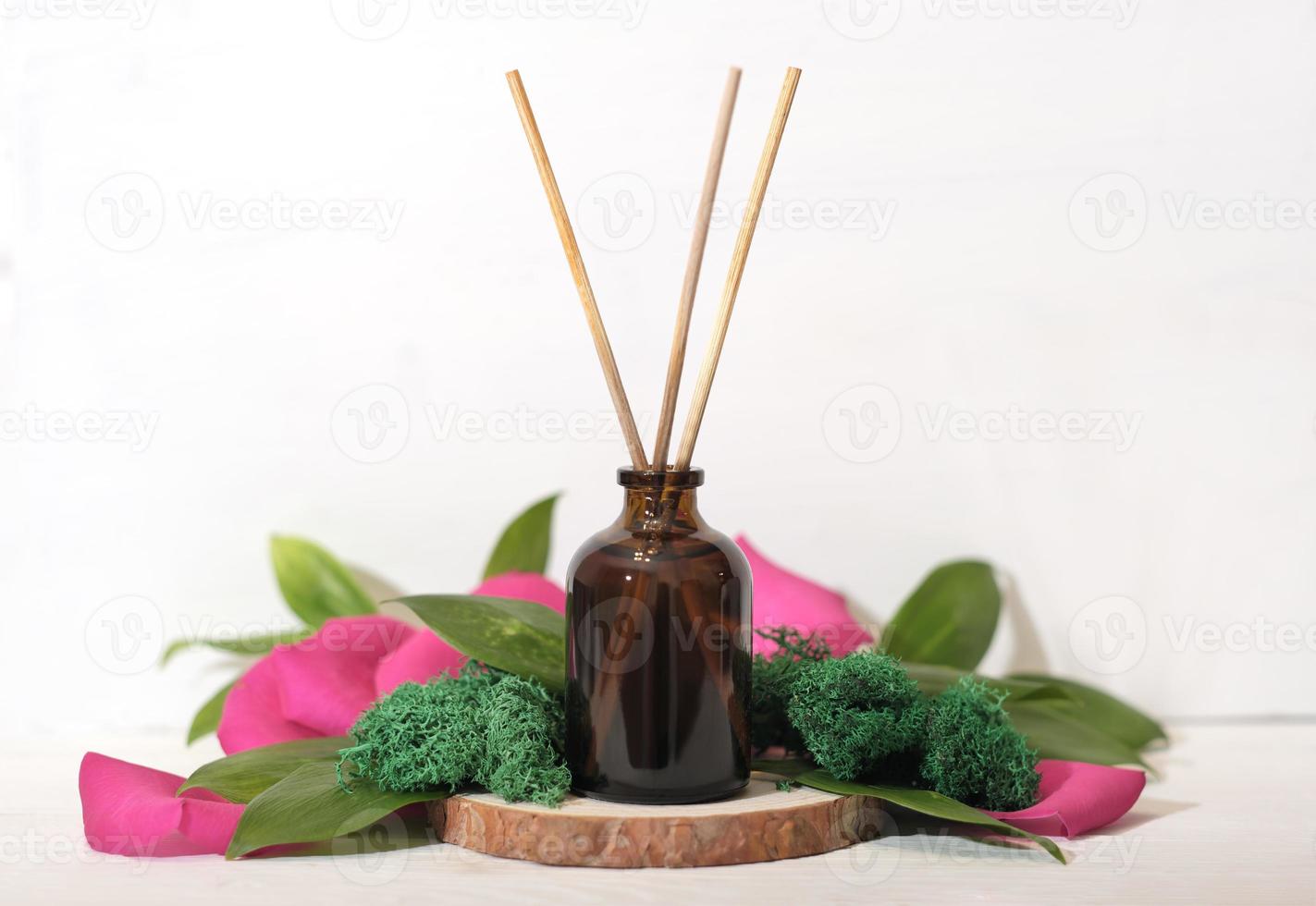 home scent, reed diffuser on wooden podium with green leaves and petals decor. floral fragrance for house ambience. photo