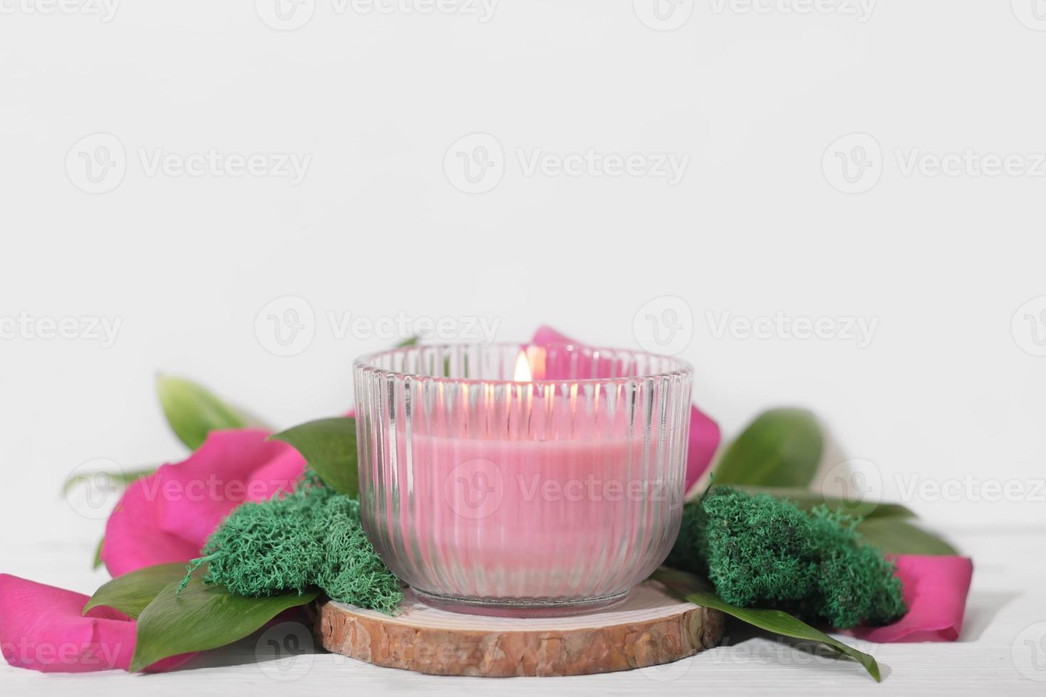 Vela de cera de soja a base de plantas veganas en tarro de cristal. vela rosa vegetariana hecha de cera de soja natural en podim de madera con decoración floral. foto