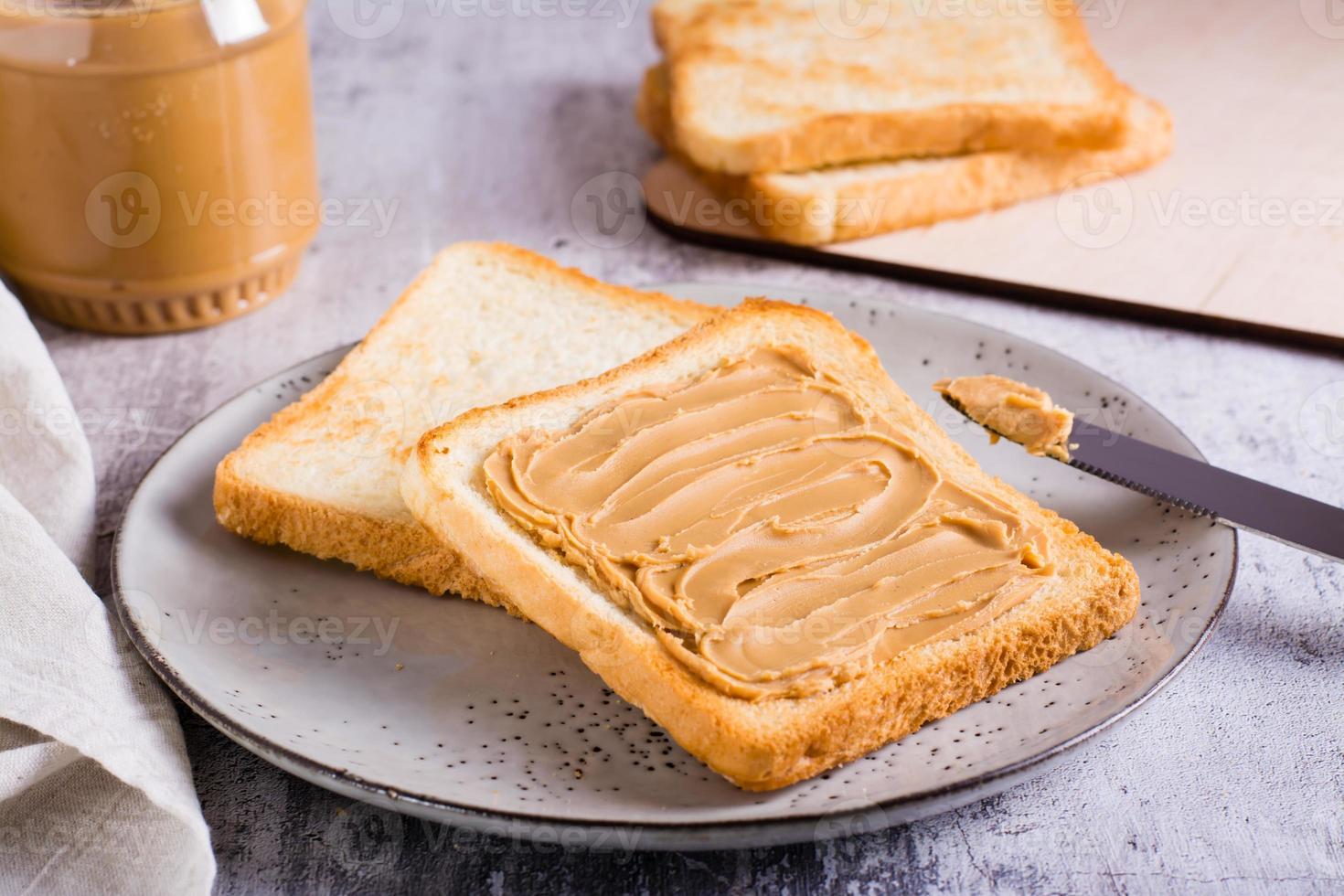 Sándwich de mantequilla de maní en pan tostado en un plato y tarro de mantequilla en la mesa foto