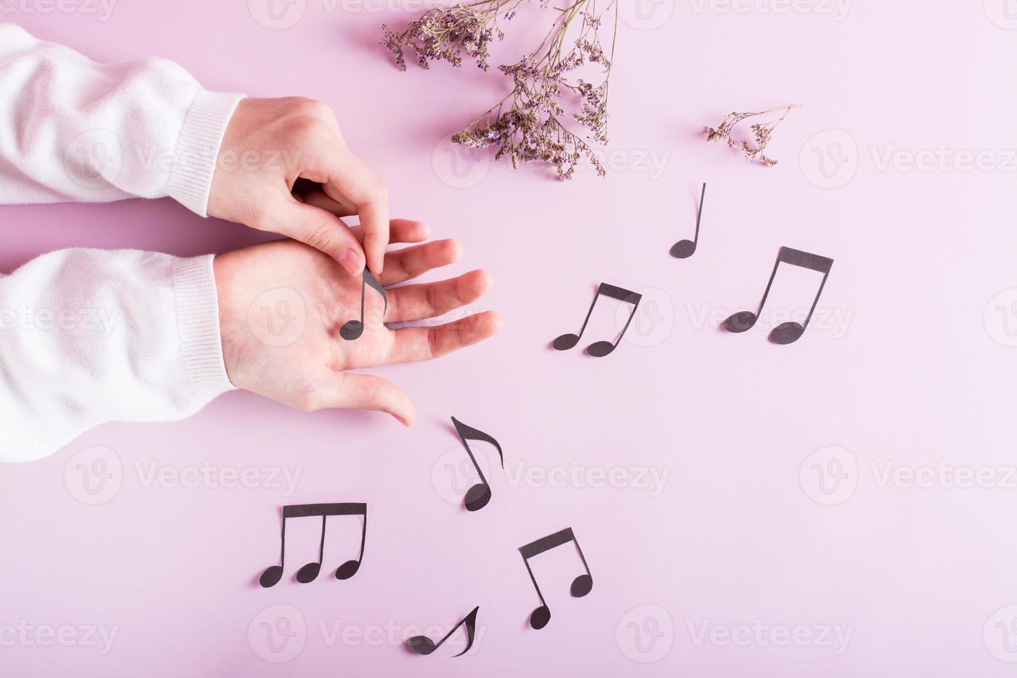 Children's hands touch paper notes and notes around on a pink background. Music education. Top view. photo