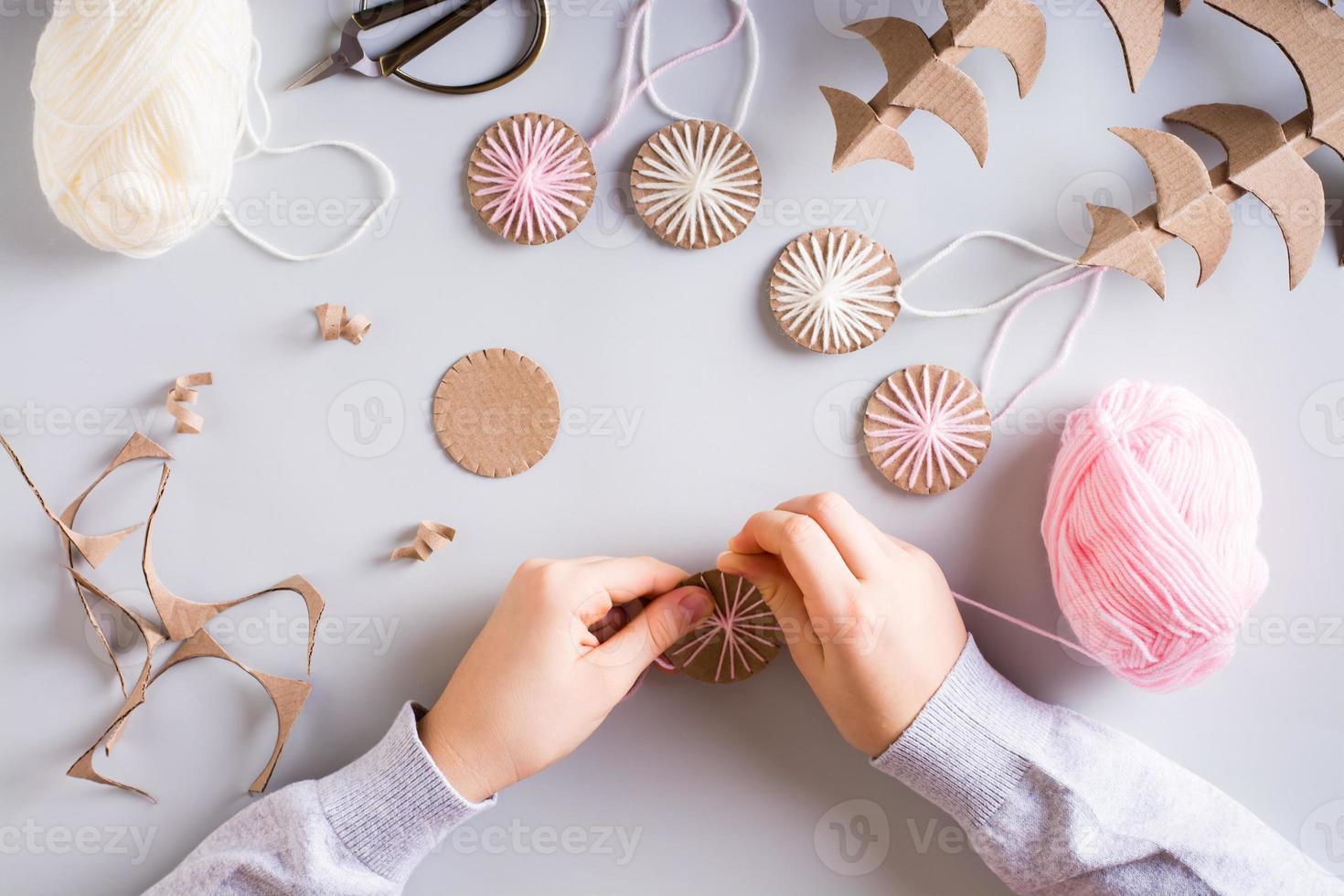 Children's hands wrap yarn on a cardboard circle for DIY Christmas handmade decorations. Top view. photo