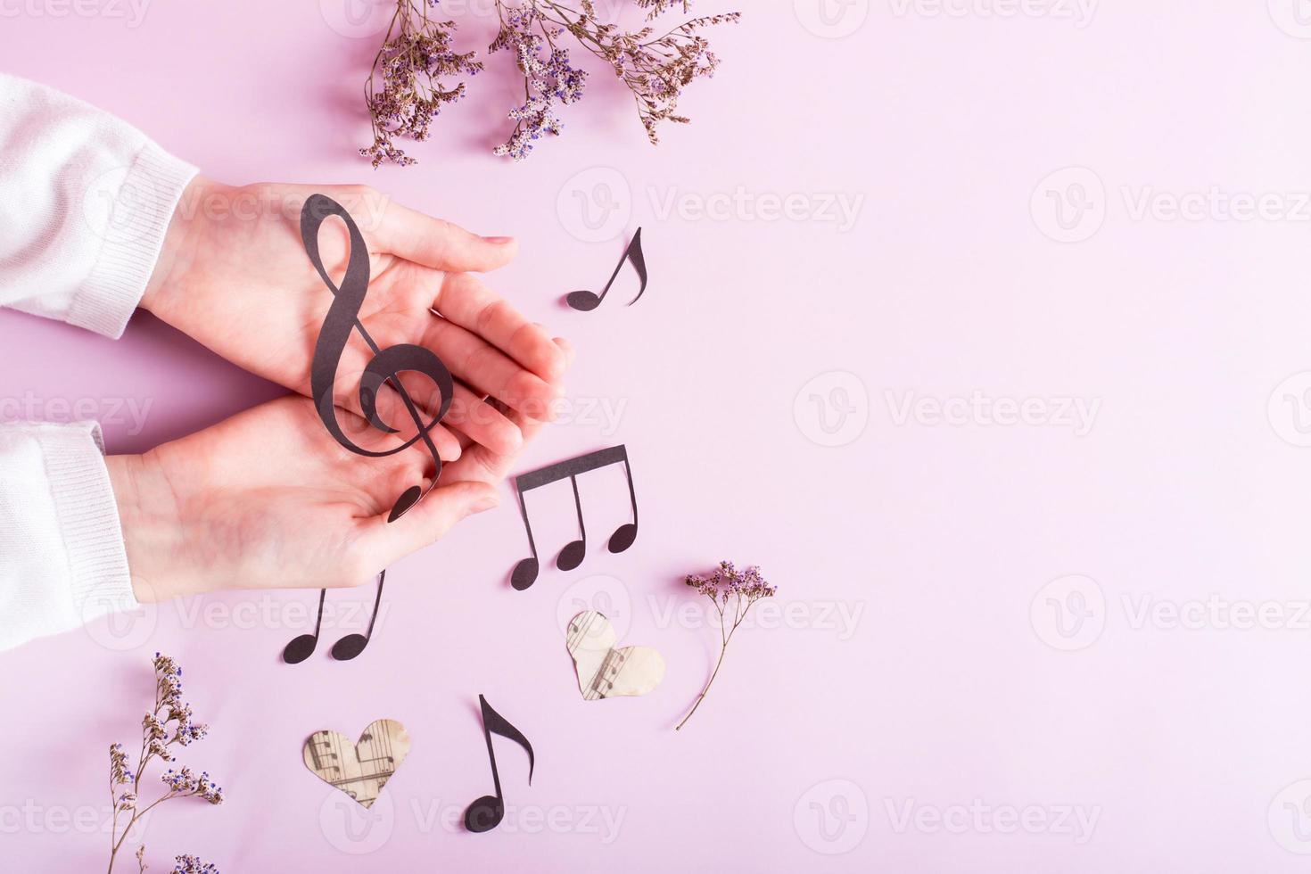 Paper musical clef in children's hands and paper notes on pink. Music education. Top view. photo