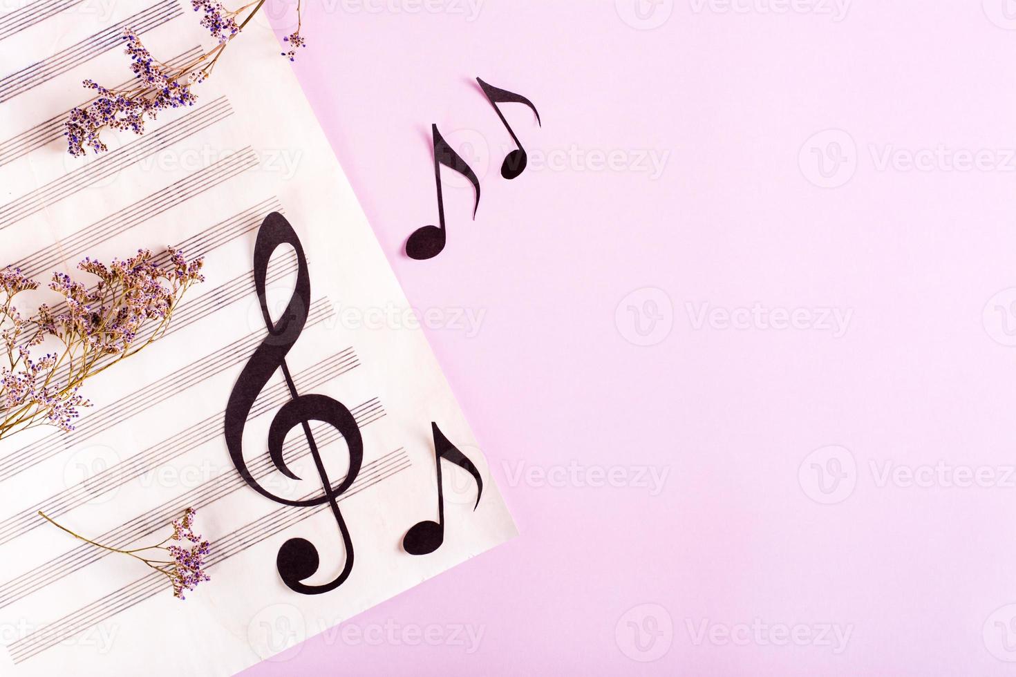 Paper musical clef and paper notes on a sheet of music and dry flowers. Top view. photo