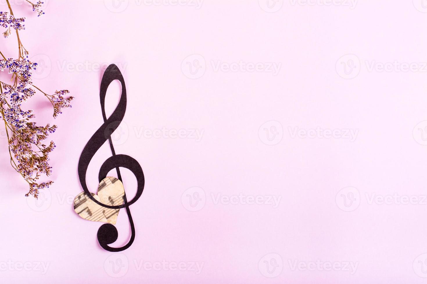 clave musical de papel, corazón y flores secas sobre un fondo rosa. vista superior. foto