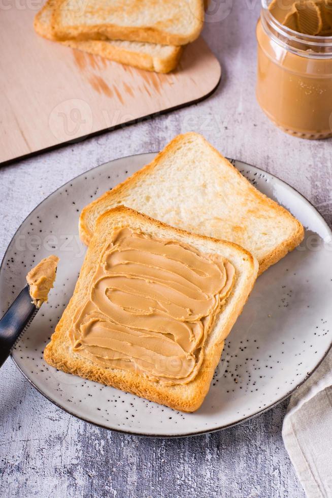 Bread toast with peanut butter on a plate and a jar of butter on the table. Vertical view photo