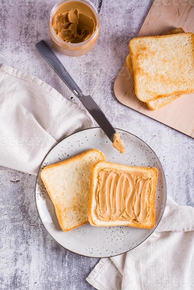 Bread toast with peanut butter on a plate and a jar of butter on the table. Top and vertical view photo